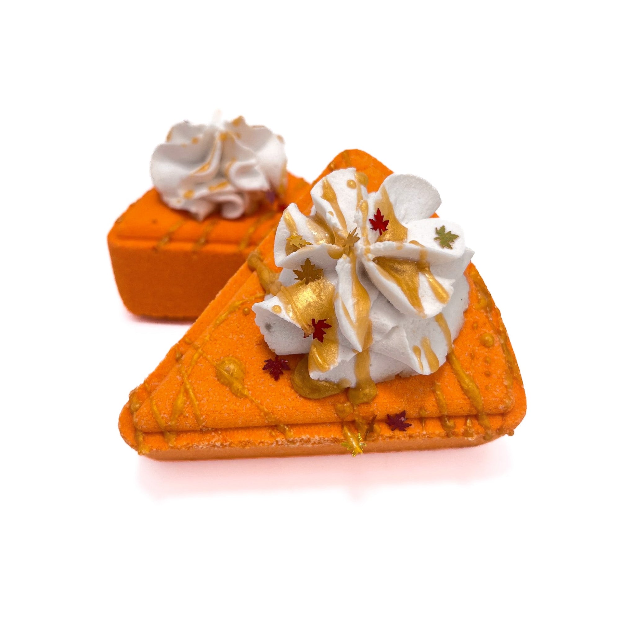 Two orange pie slice shaped bath bombs topped with white bubble bar, drizzle with light orange soap.