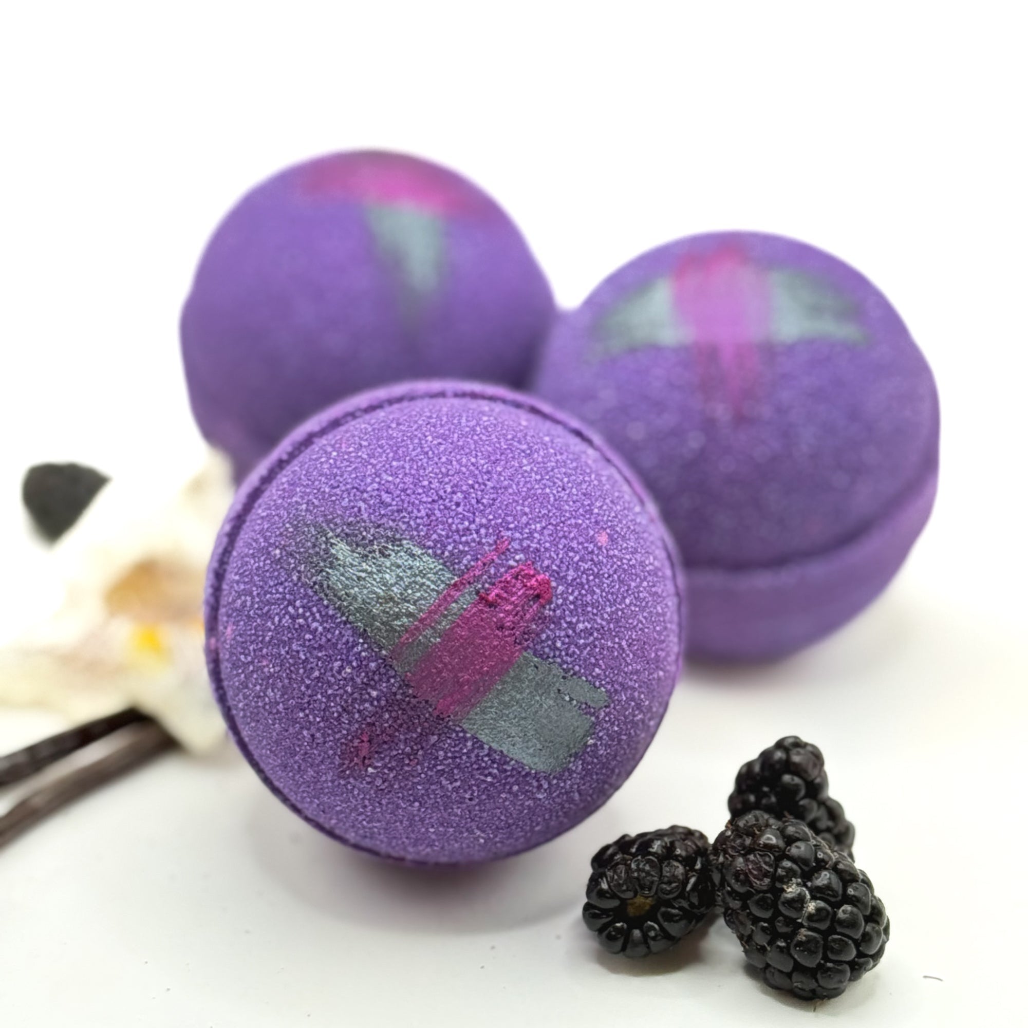 Three purple raspberry vanilla bath bombs with a butterfly design on a white background with blackberries.