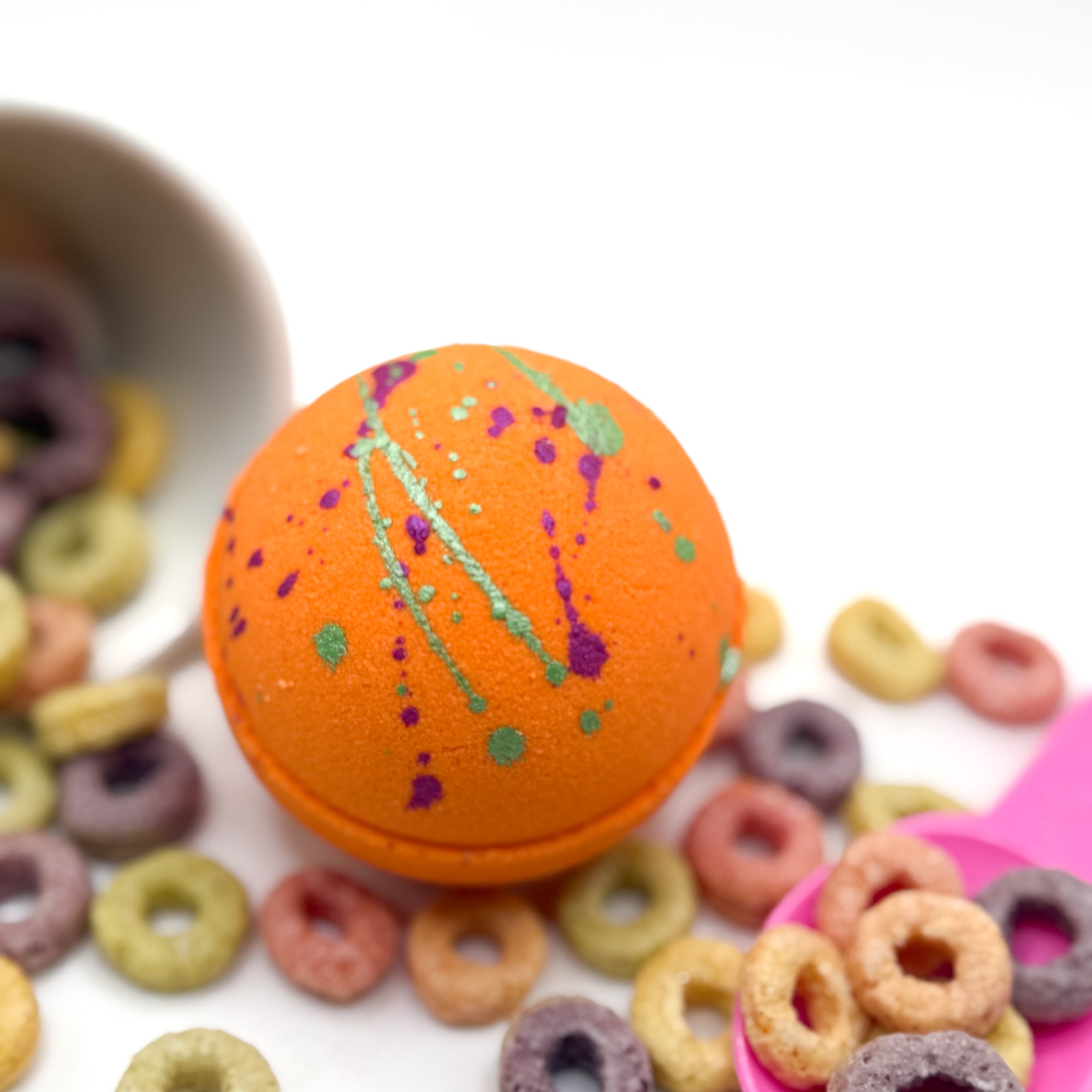 Round bright orange bath bomb splattered with green and purple mica.