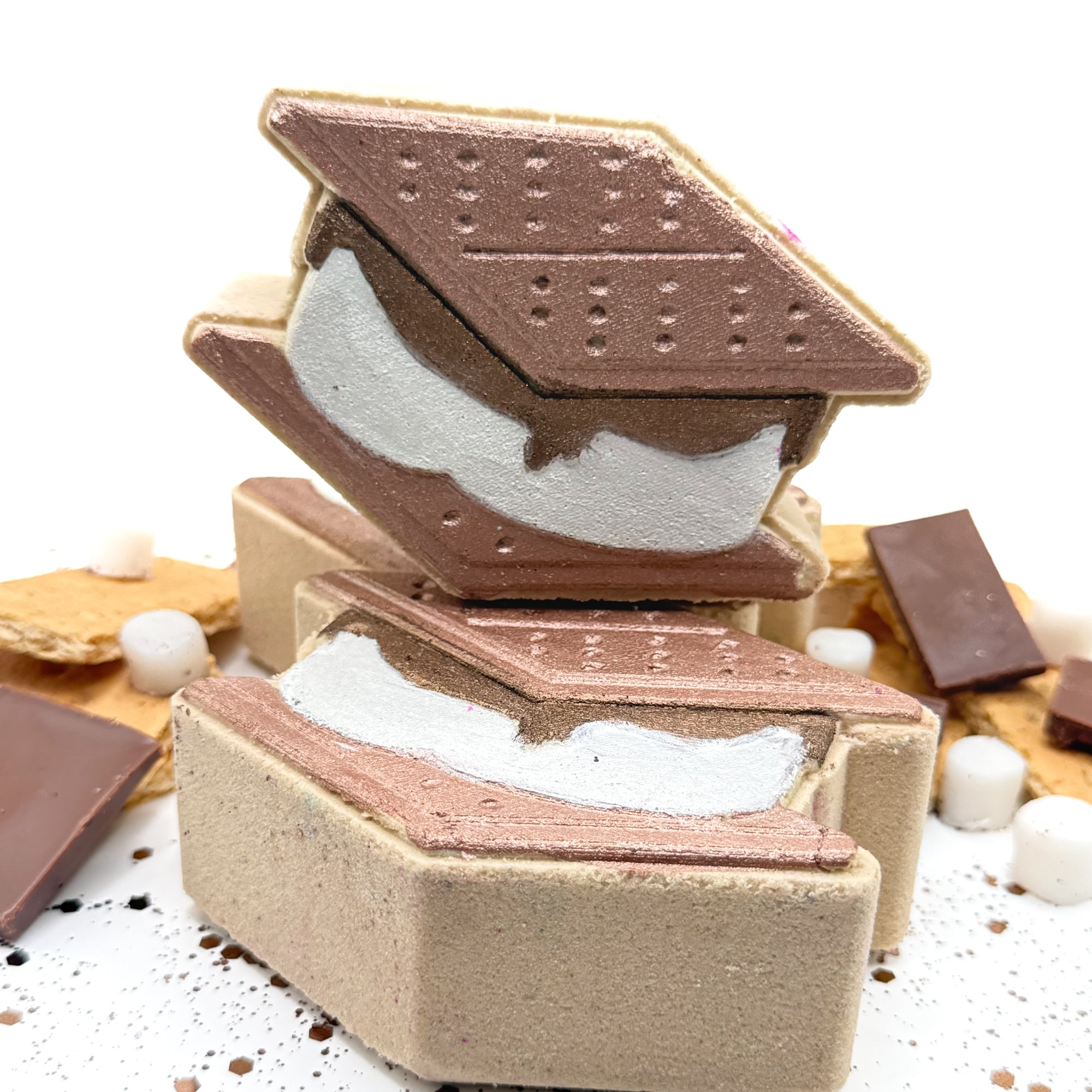 Two hand painted S’mores shaped bath bomb with s’mores decorations around them on a white background.
