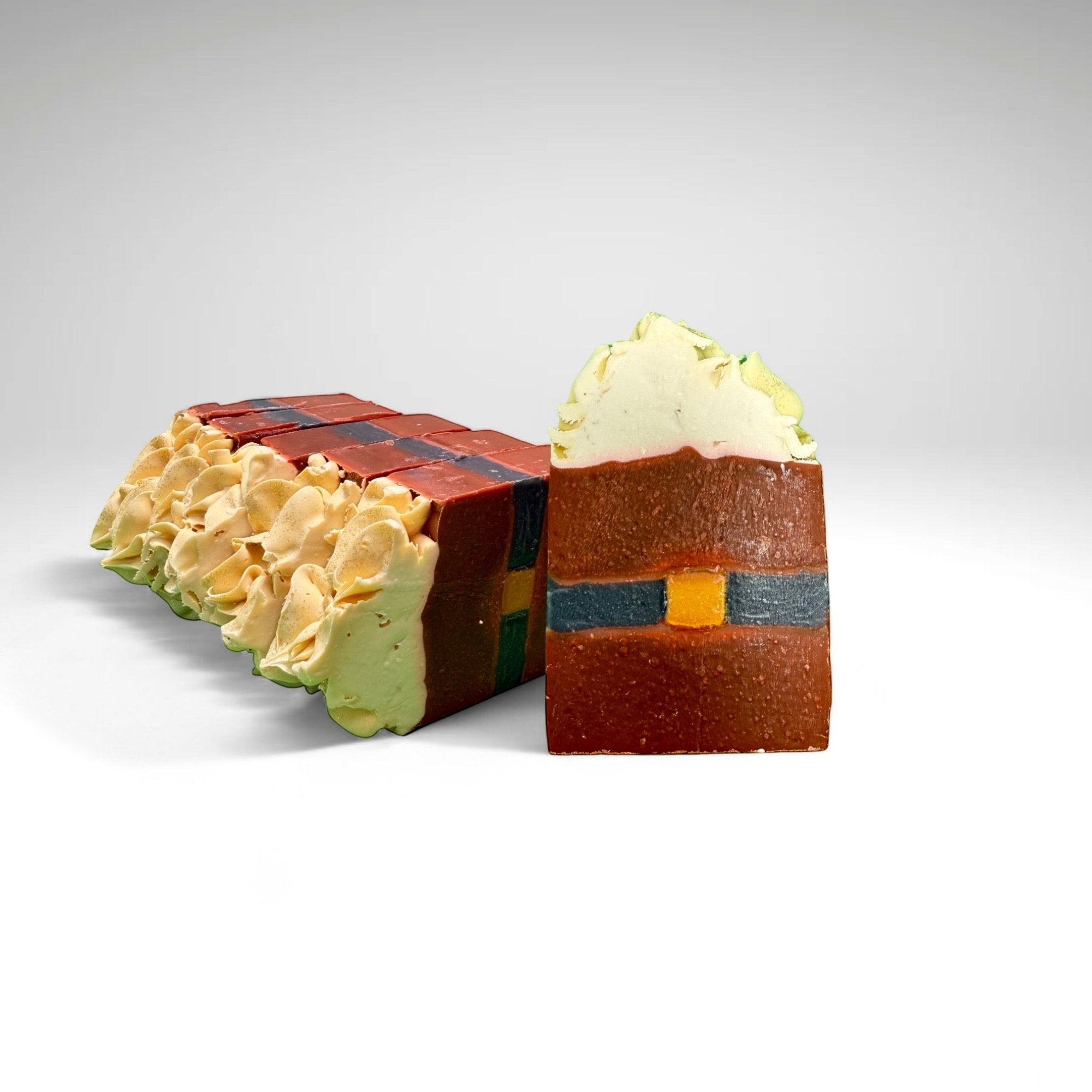 Several bars of Rusted Acre Soap Company's Santa Belt bar soap. Red bar with black line through center with gold. Topped with white soap.