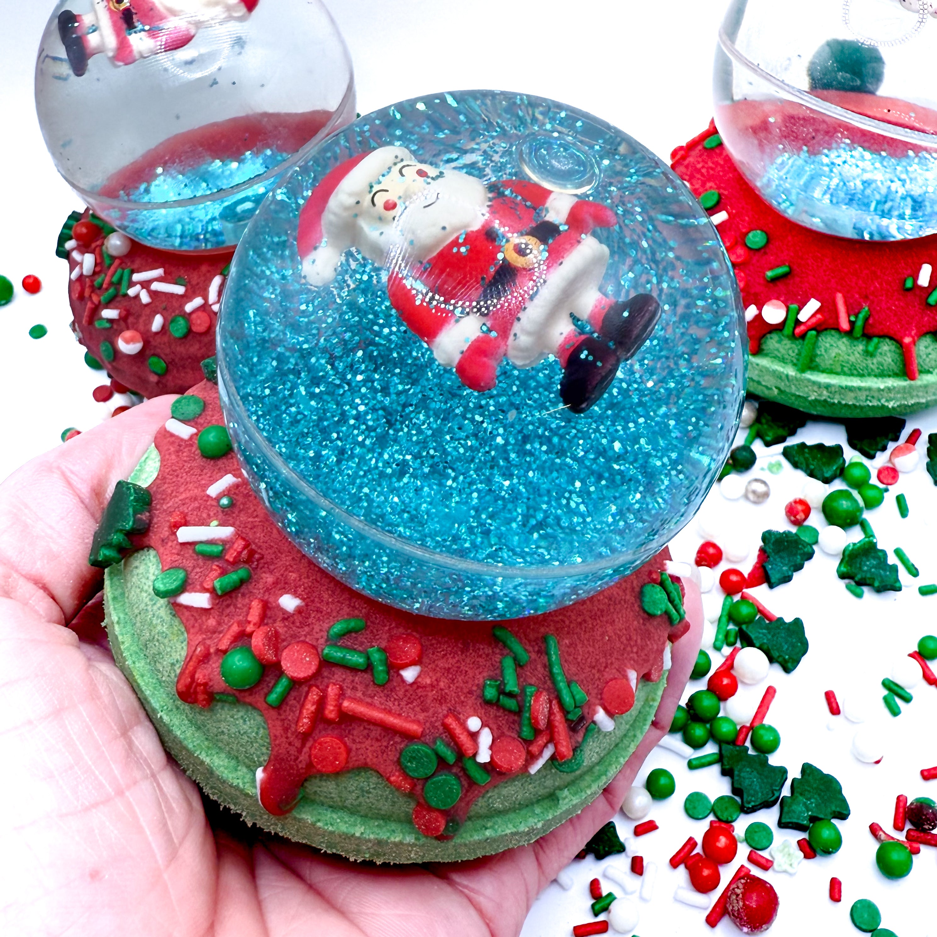 A Santa snow globe bath bomb with a Santa Claus bouncy ball in a hand on a festive background.