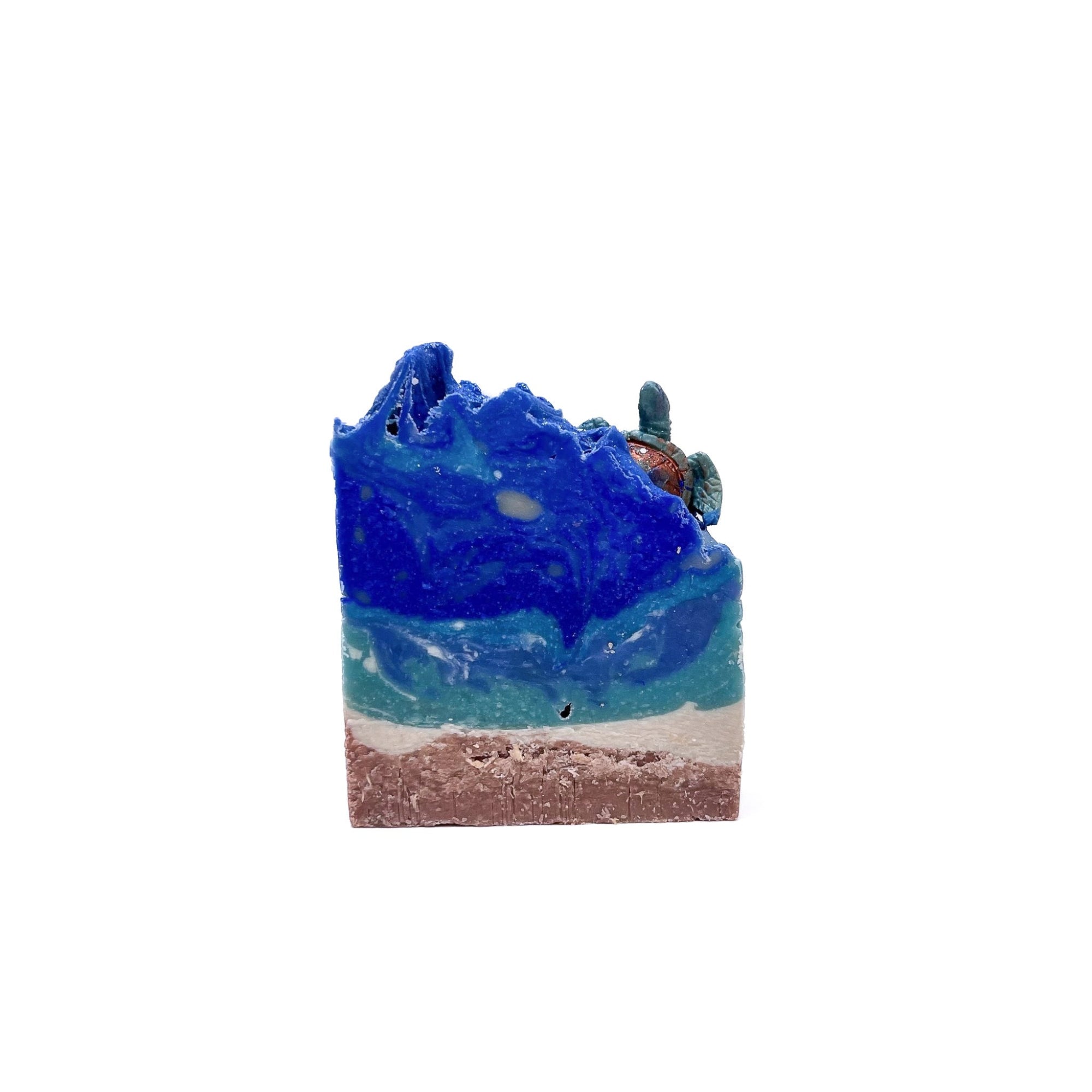 A bar of Sea Turtle handmade soap. Tan on the bottom for sand, swirled turquoise and blue for water. Topped with a sea turtle soap embed.