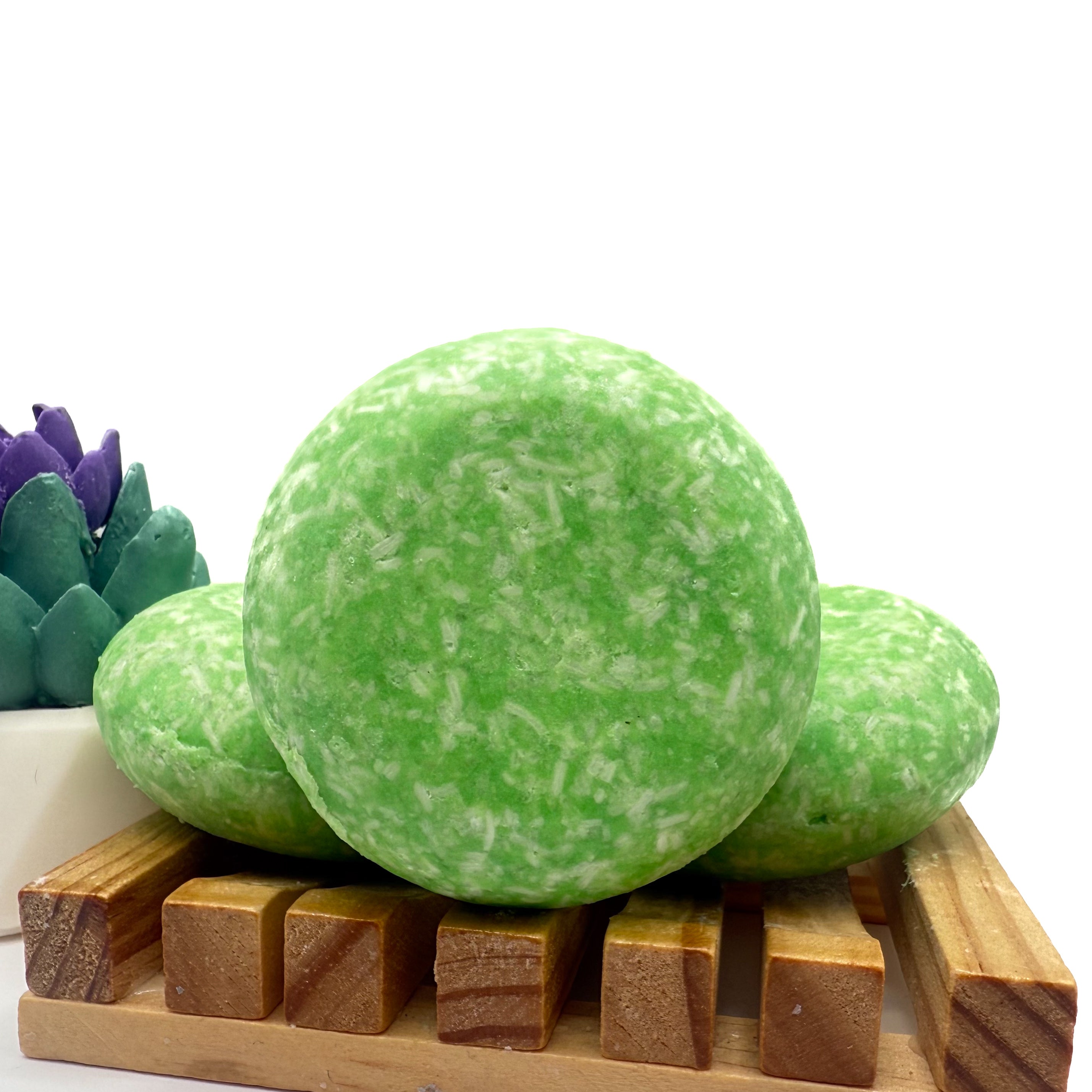 Three coconut lime cooler shampoo bars sitting on a wood soap dish two laying flat, one standing up.