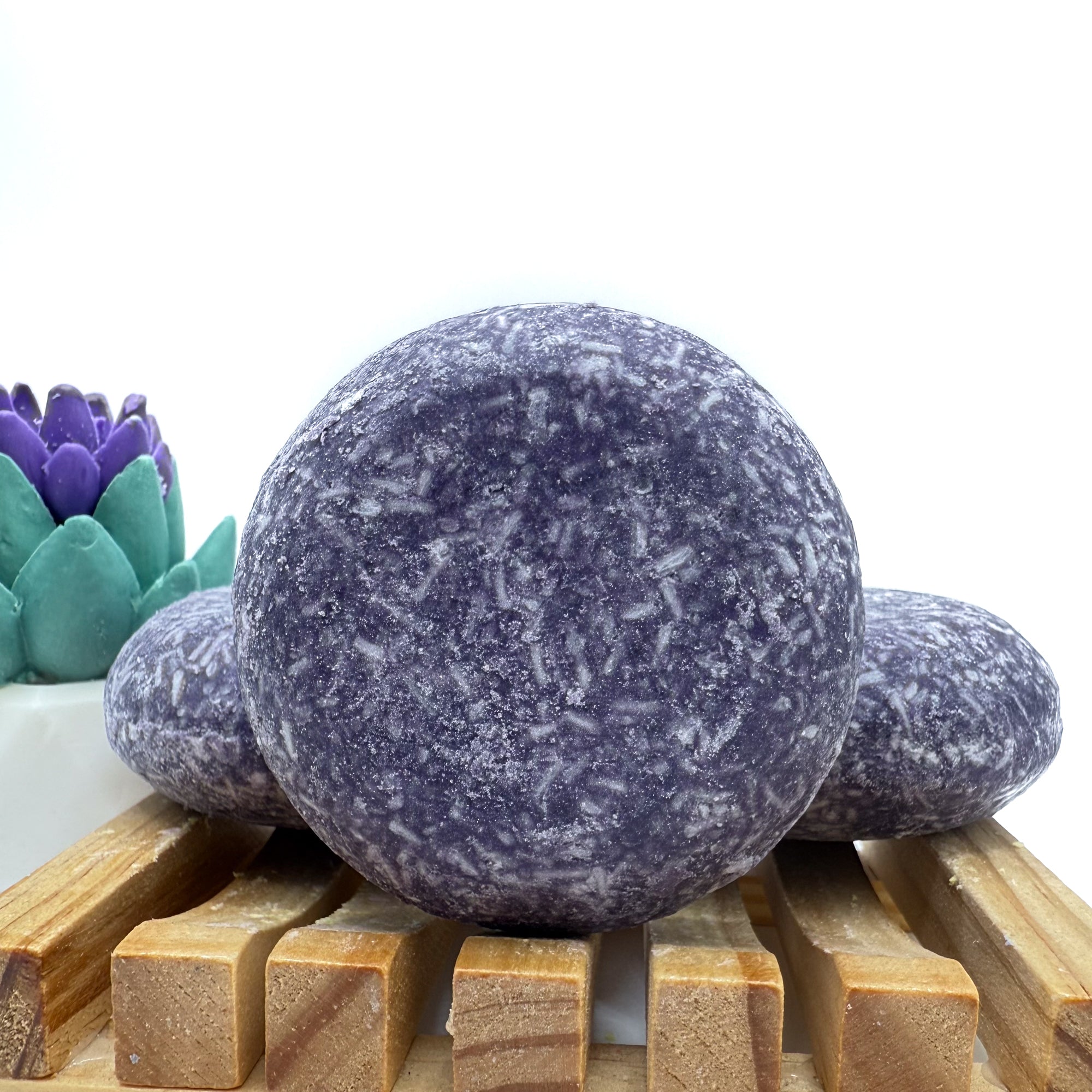 Three enchanted shampoo bars sitting on a wood soap dish two laying flat, one standing up.