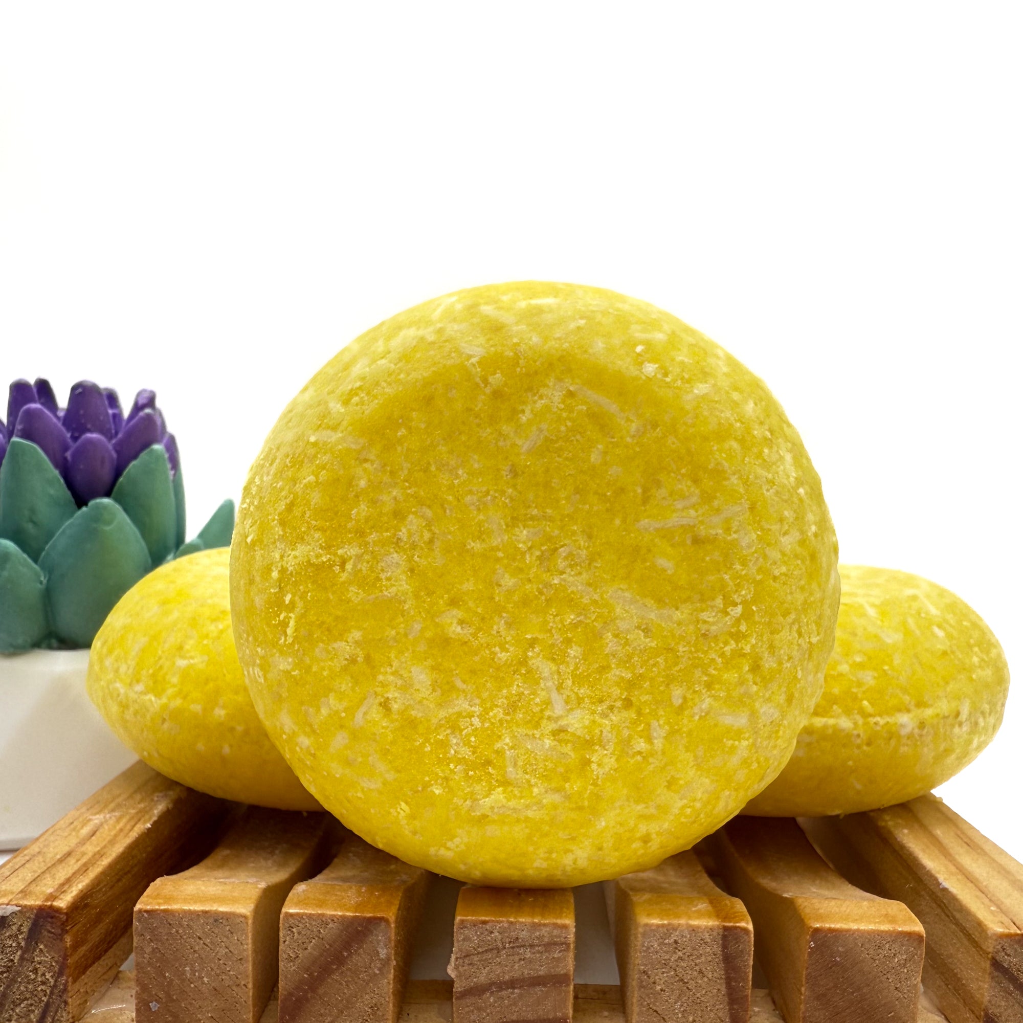 Three lemon love shampoo bars sitting on a wood soap dish two laying flat, one standing up.