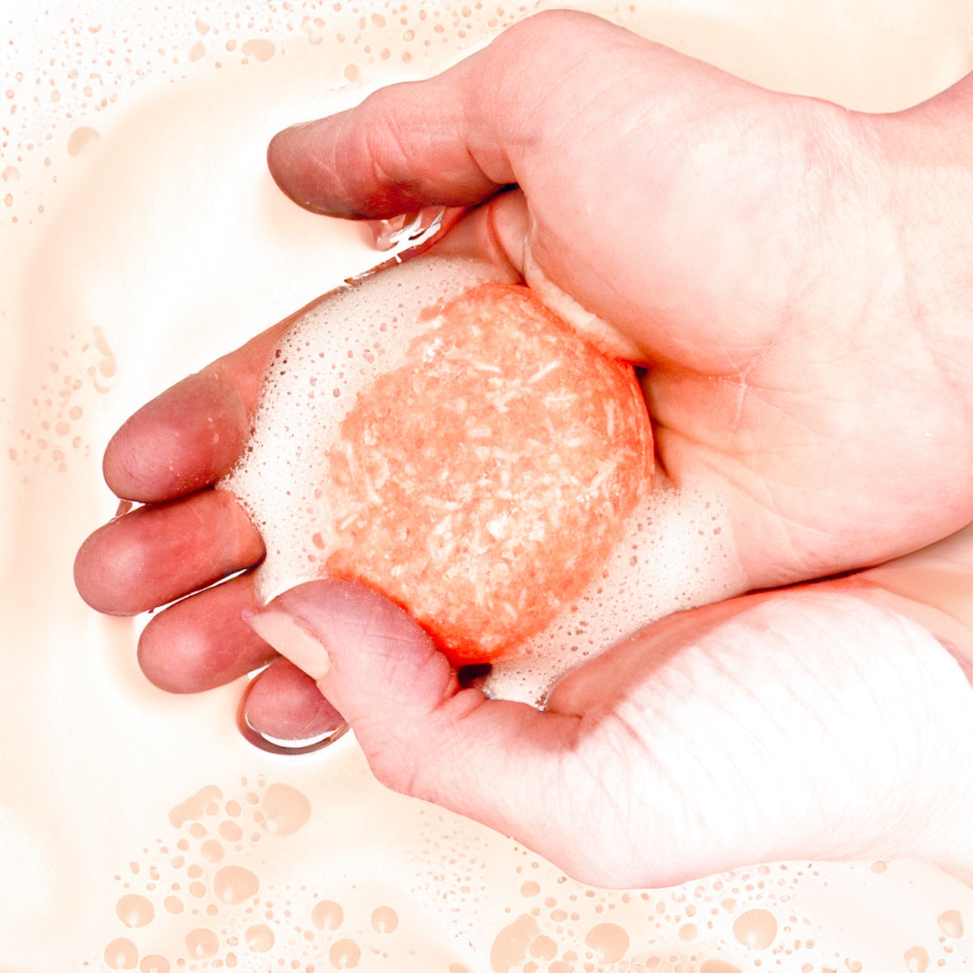 Light orange solid shampoo bar lathered in hand overtop of foamy water.
