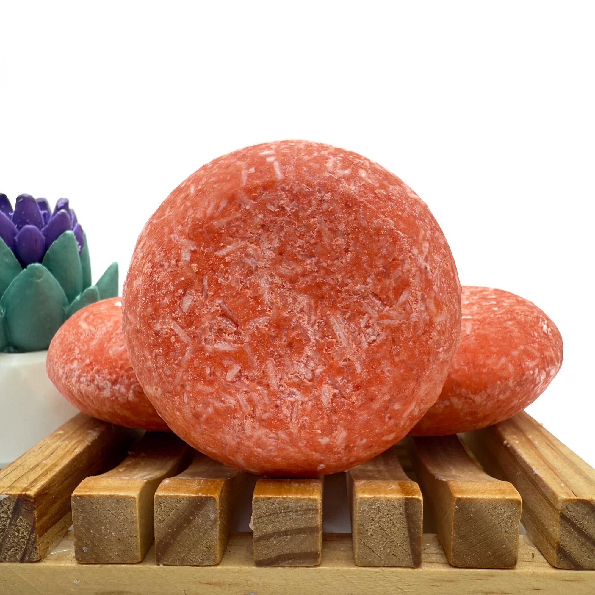 Three mango tango shampoo bars sitting on a wood soap dish two laying flat, one standing up.