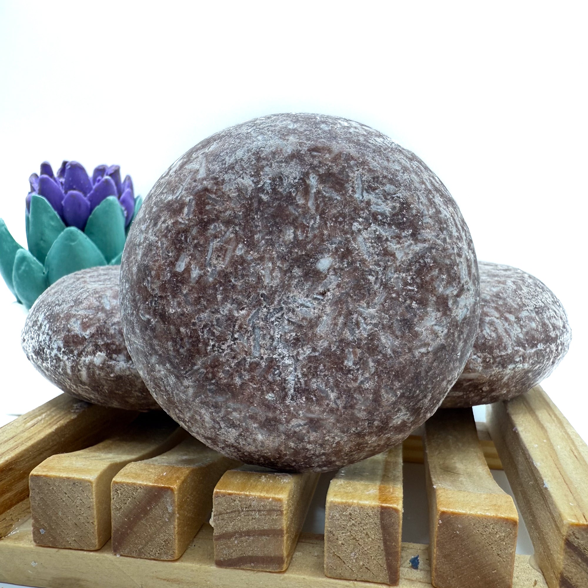 Three moroccan spice shampoo bars sitting on a wood soap dish two laying flat, one standing up.