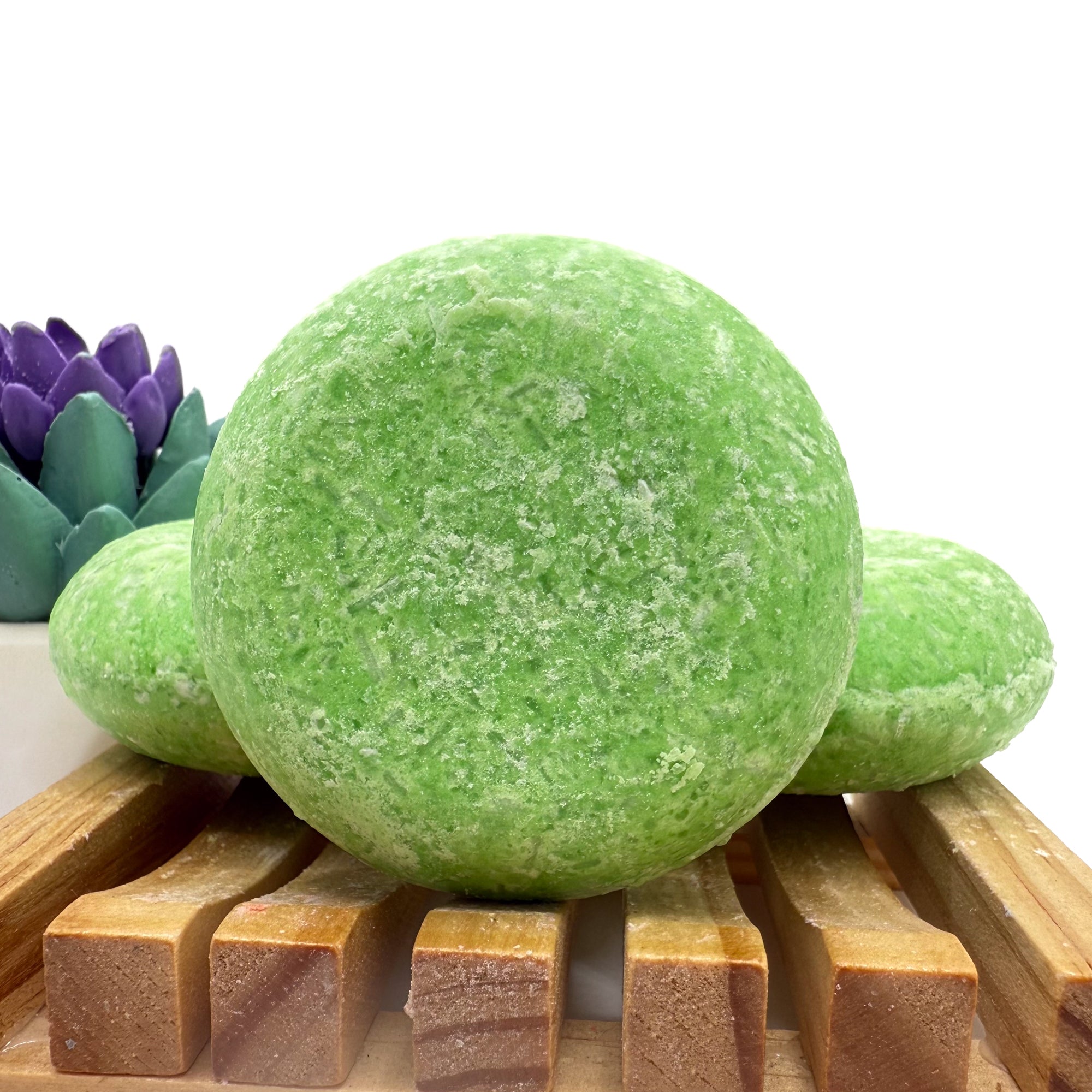 Three summer melon shampoo bars sitting on a wood soap dish two laying flat, one standing up.