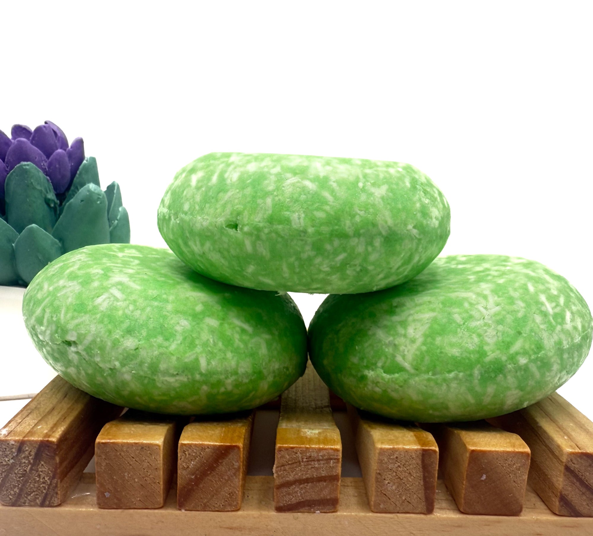 Three Coconut Lime Cooler shampoo bars sitting on. wood soap dish stacked on top of each other.