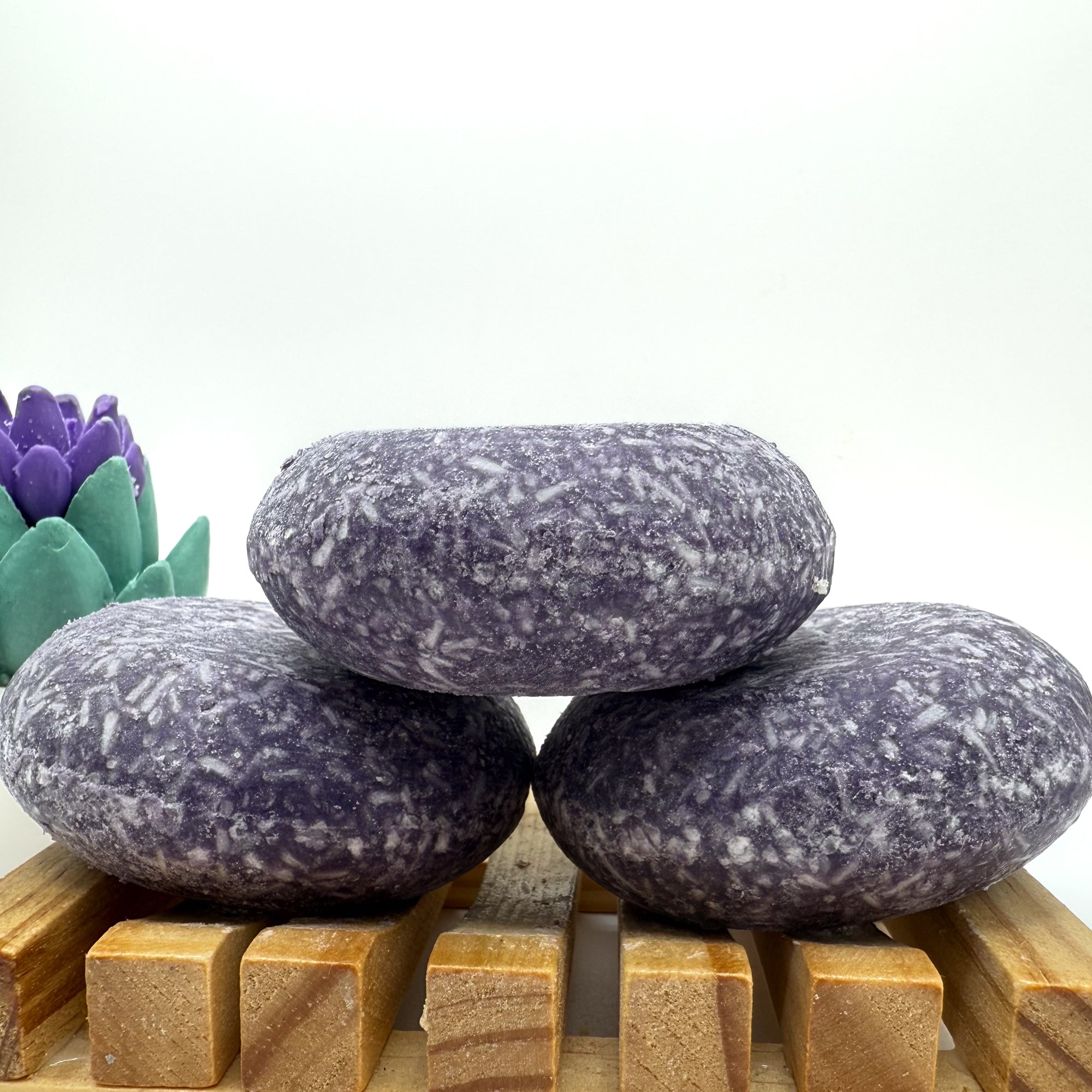 Three enchanted shampoo bars sitting on. wood soap dish stacked on top of each other.