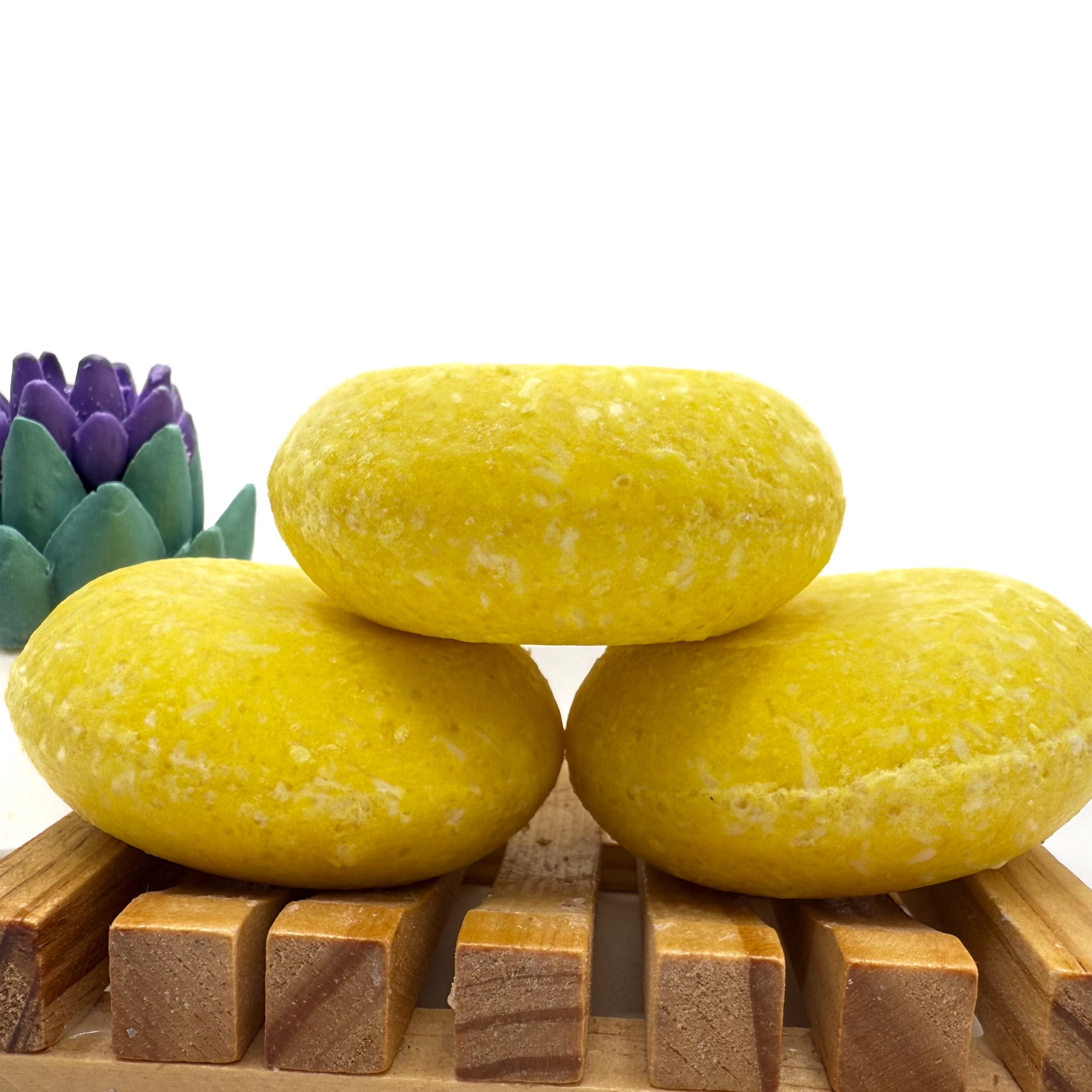 Three lemon love shampoo bars sitting on. wood soap dish stacked on top of each other.