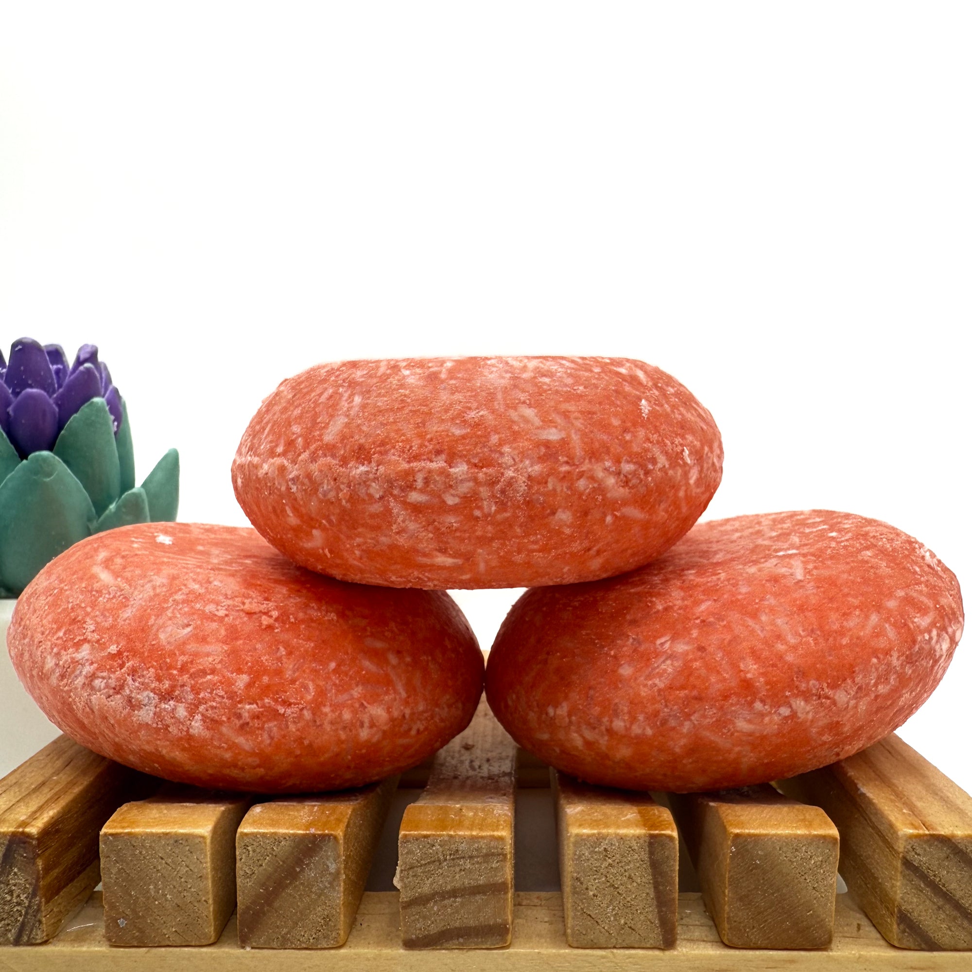 Three mango tango shampoo bars sitting on. wood soap dish stacked on top of each other.