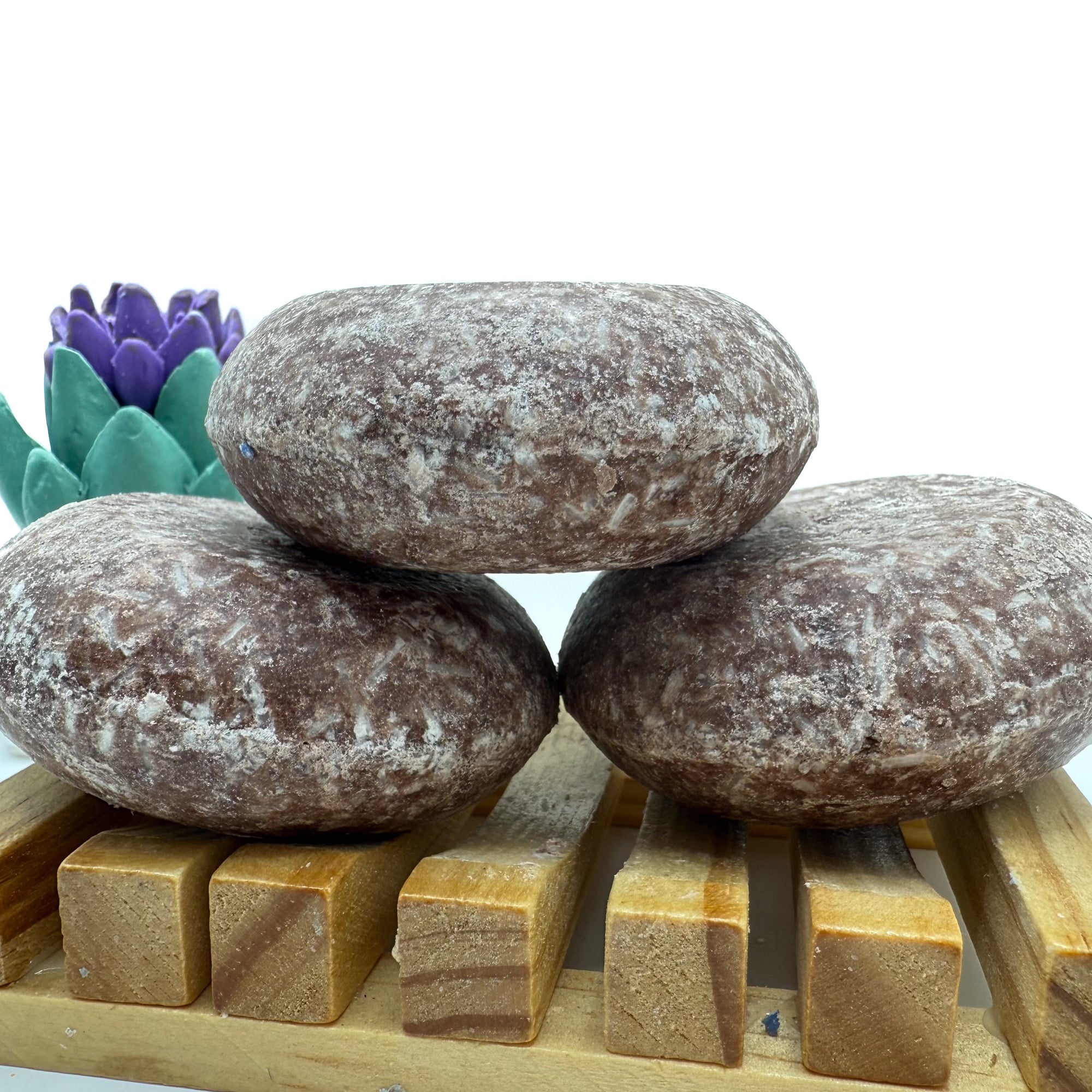 Three moroccan spice shampoo bars sitting on. wood soap dish stacked on top of each other.