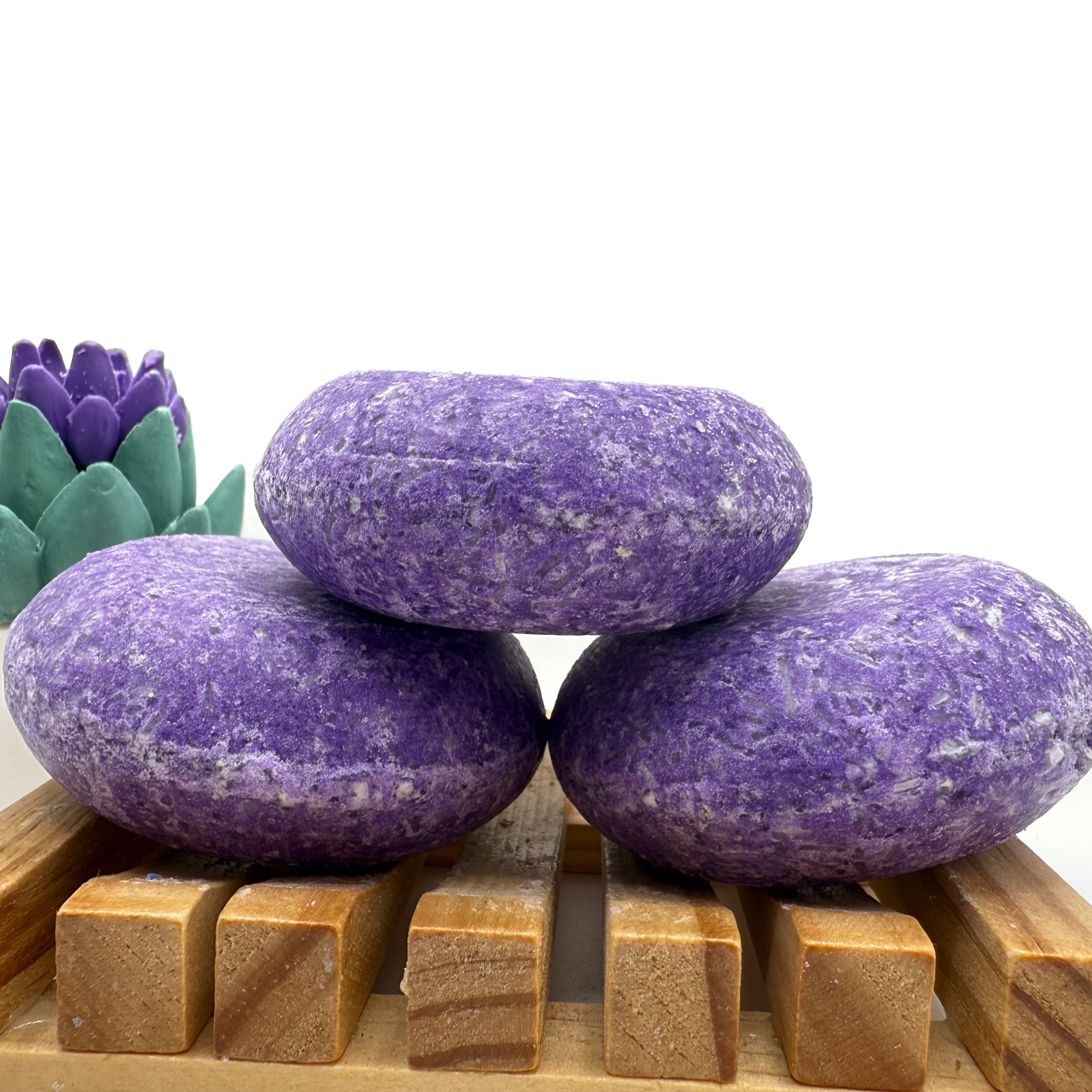 Three Pomegranate Kiss shampoo bars sitting on. wood soap dish stacked on top of each other.