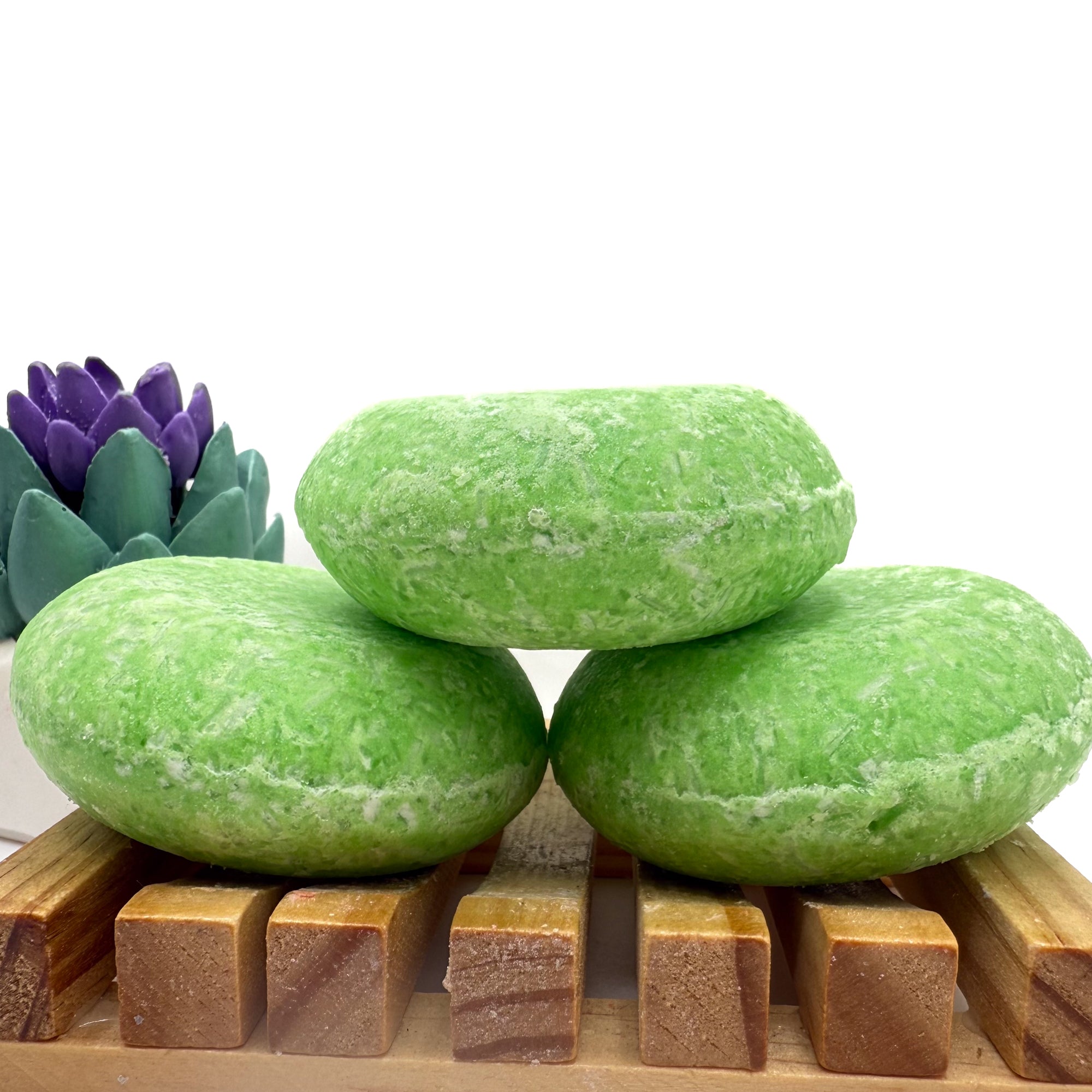 Three summer melon shampoo bars sitting on. wood soap dish stacked on top of each other.