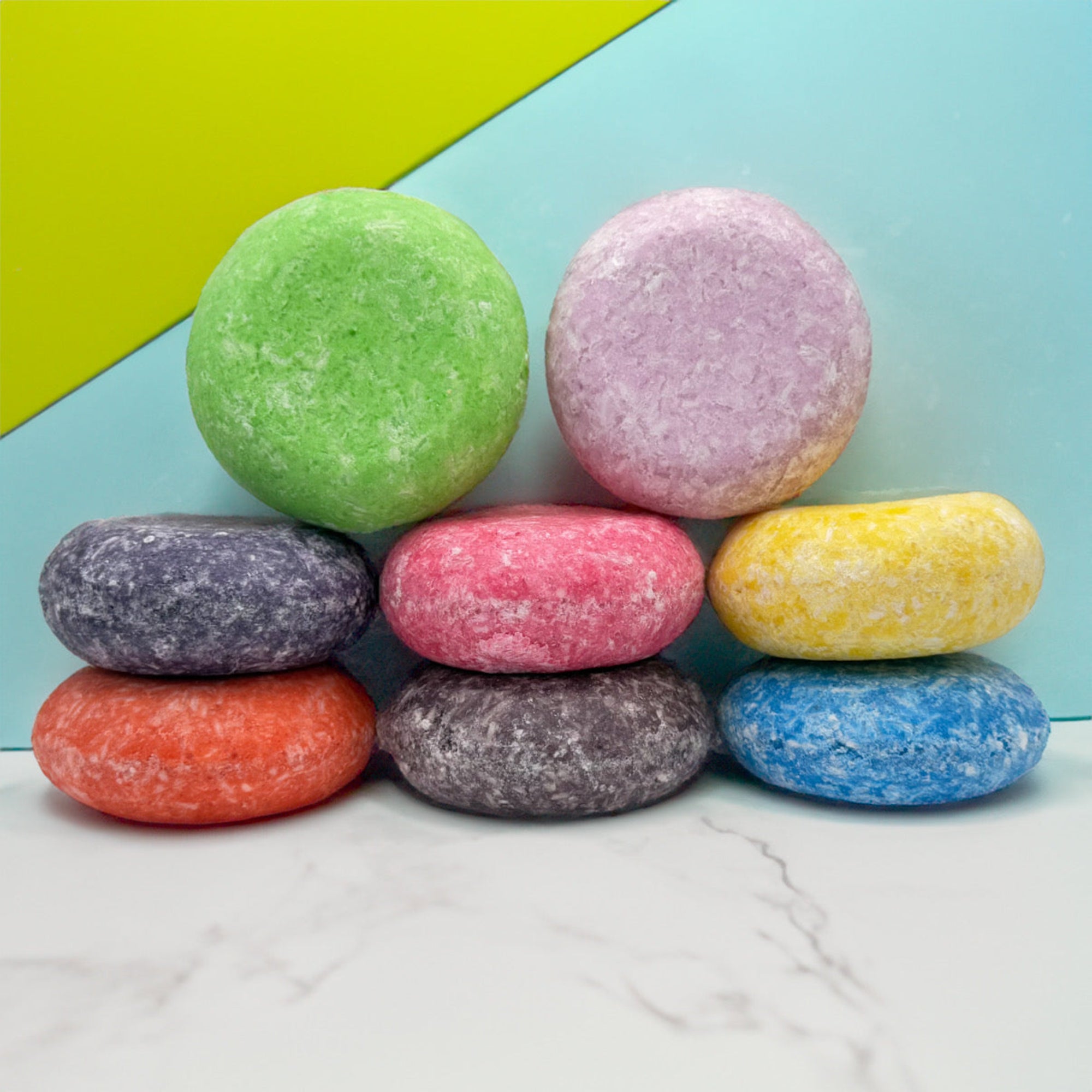 Eight multi colored solid shampoo bars stacked on top of each other on a marble counter top with a fun multi colored background.