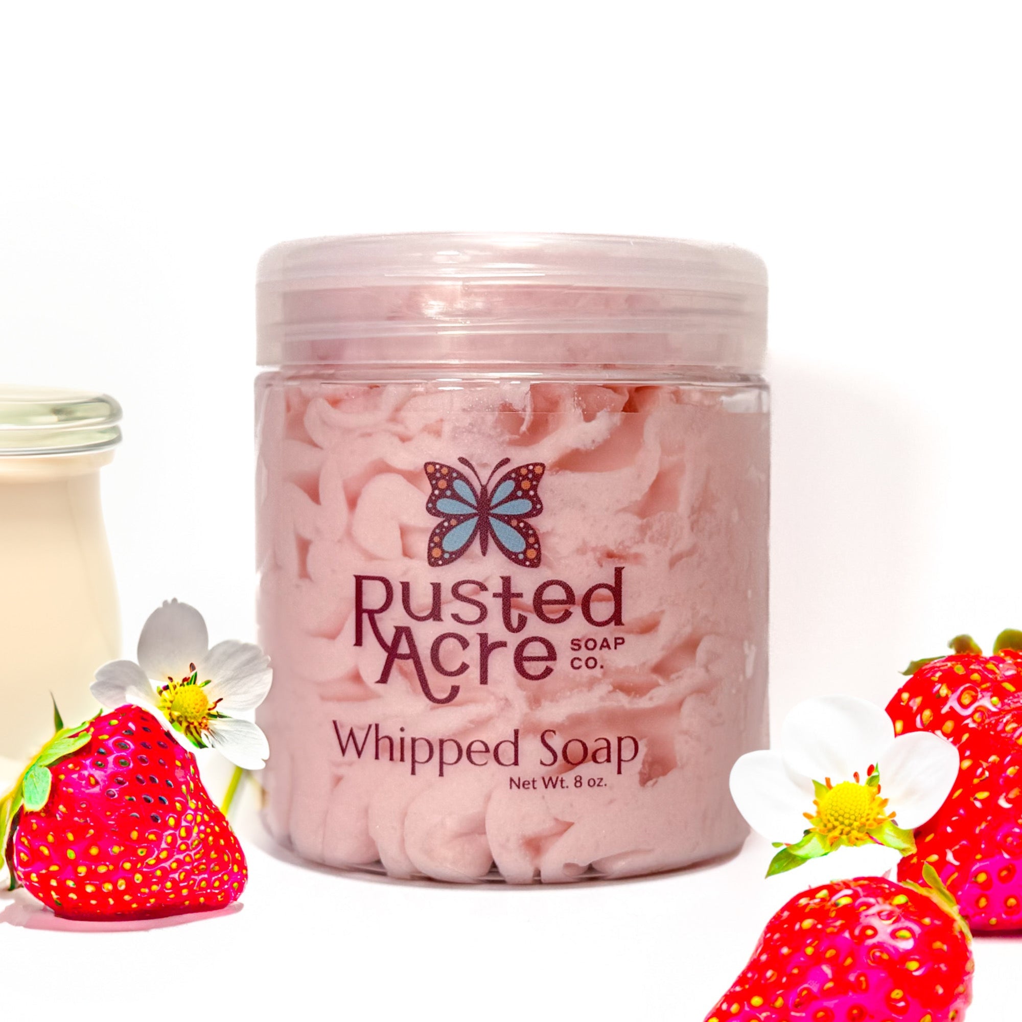 Jar of Rusted Acre Soap Company's vegan strawberries and cream whipped soap. Pink soap in a reusable plastic jar in a lifestyle setting.