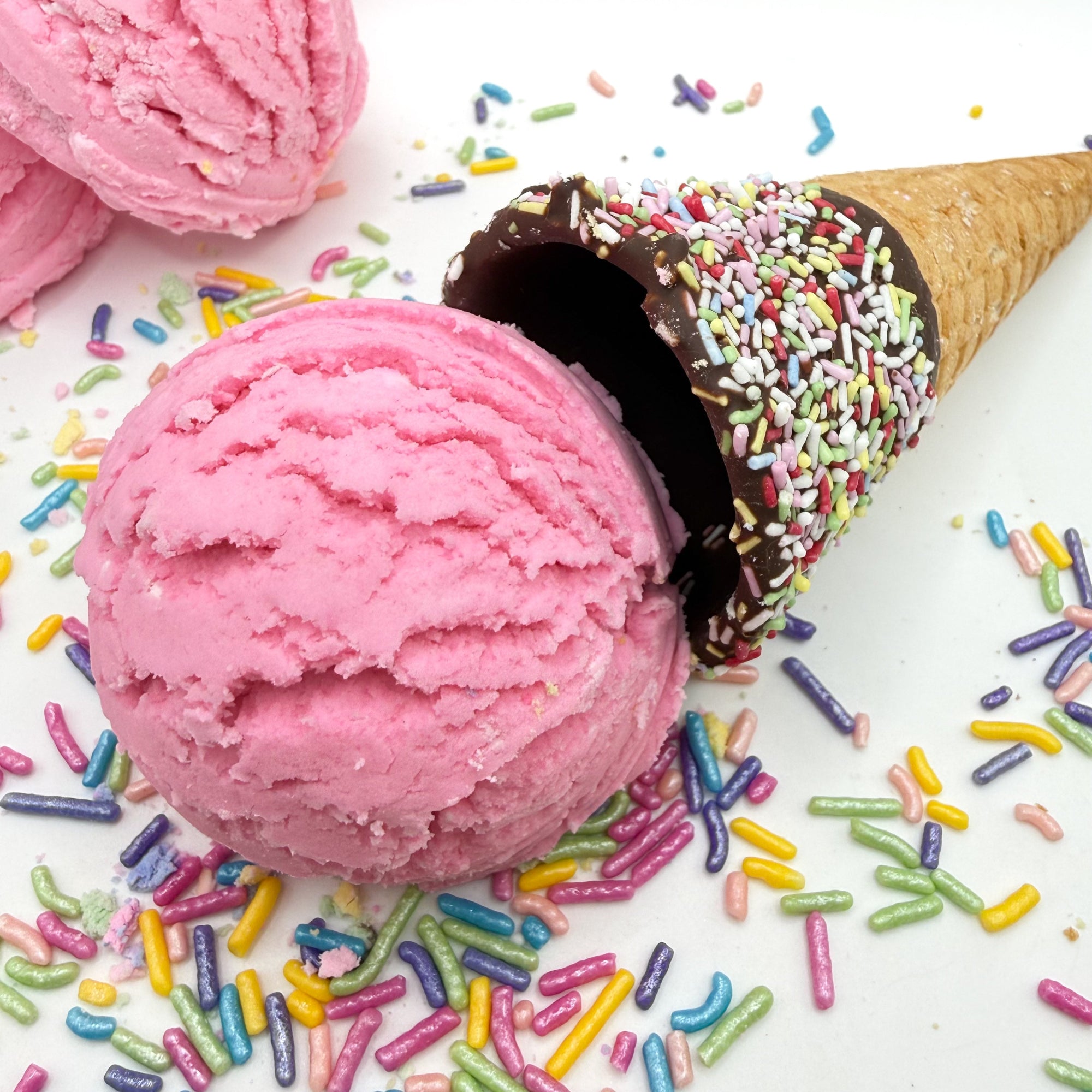 A scoop of pink solid bubble bath resembling a scoop of ice cream with chocolate covered cone and colorful sprinkles.