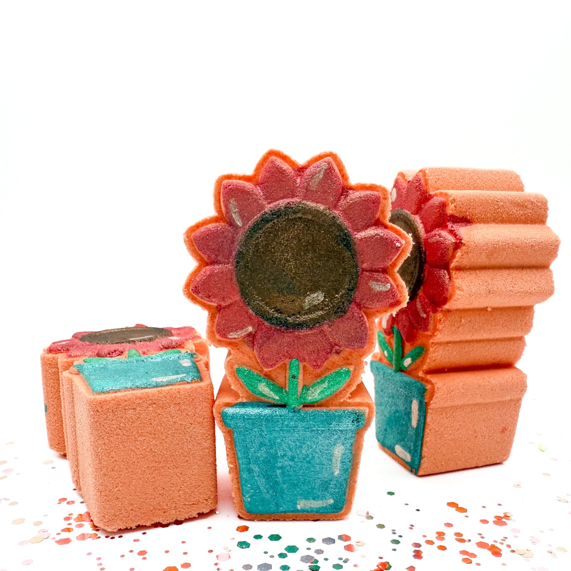 Hand painted Sunflower Pot bath bomb made by Rusted Acre Soap Company. Peach in color with a. pink/coral sunflower. Three sunflower pots standing up to show, front, side and bottom view.