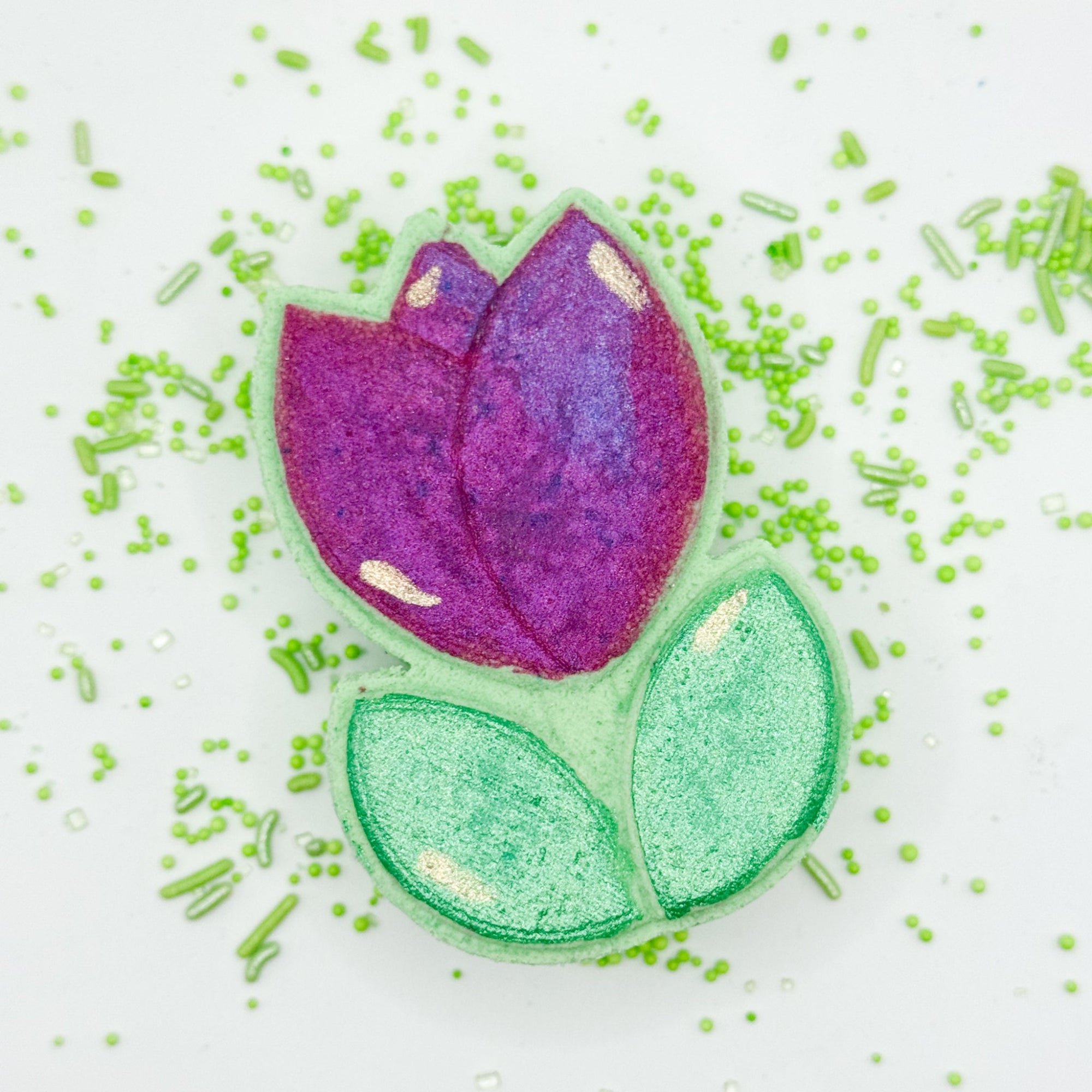 Spring Tulip bath bomb, hand painted and made by Rusted Acre Soap Co. Green and pink/purple hand painted tulip bath bomb laying flat with sprinkles around it.