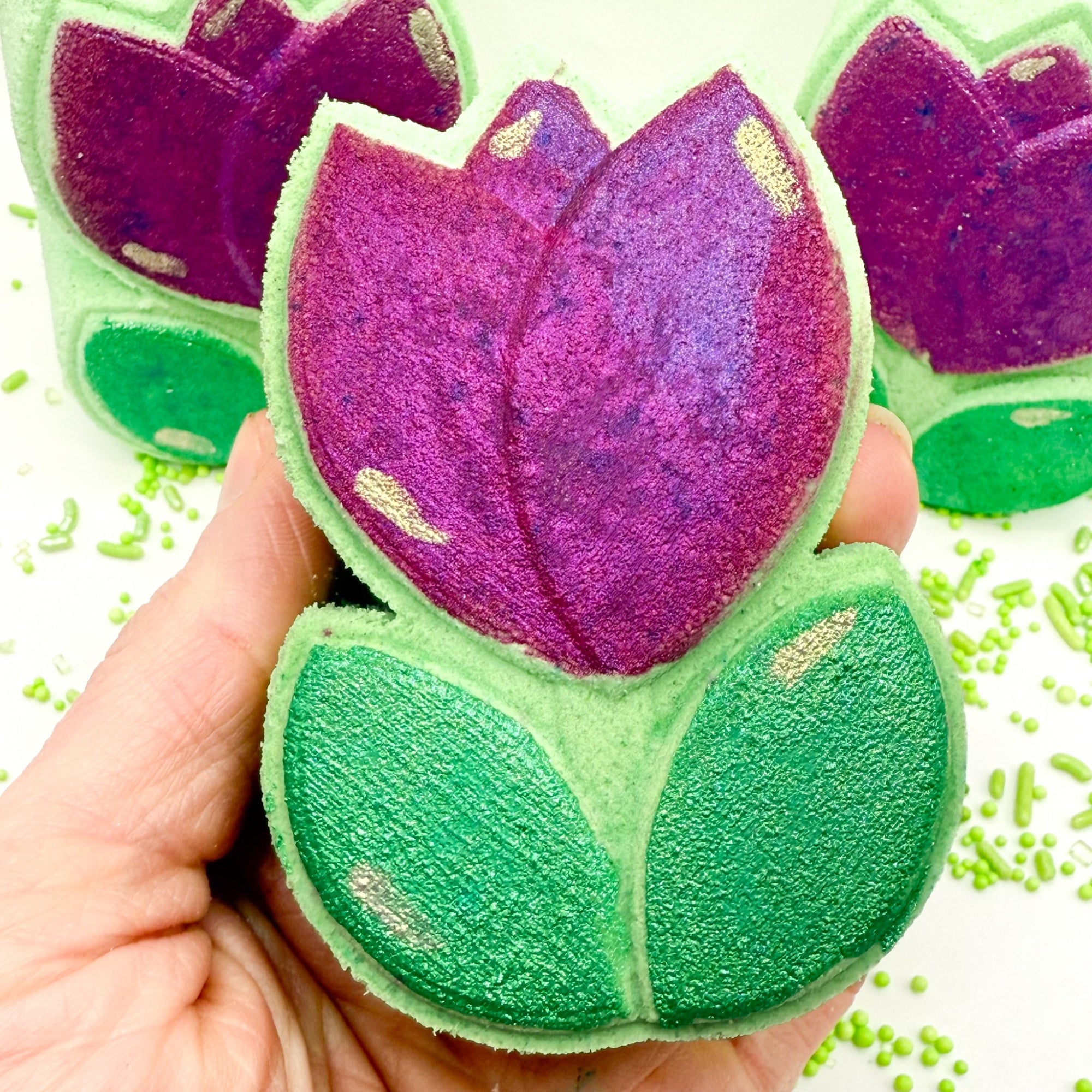 Spring Tulip bath bomb, hand painted and made by Rusted Acre Soap Co. Green and pink/purple hand painted tulip bath bomb in hand for up close look.