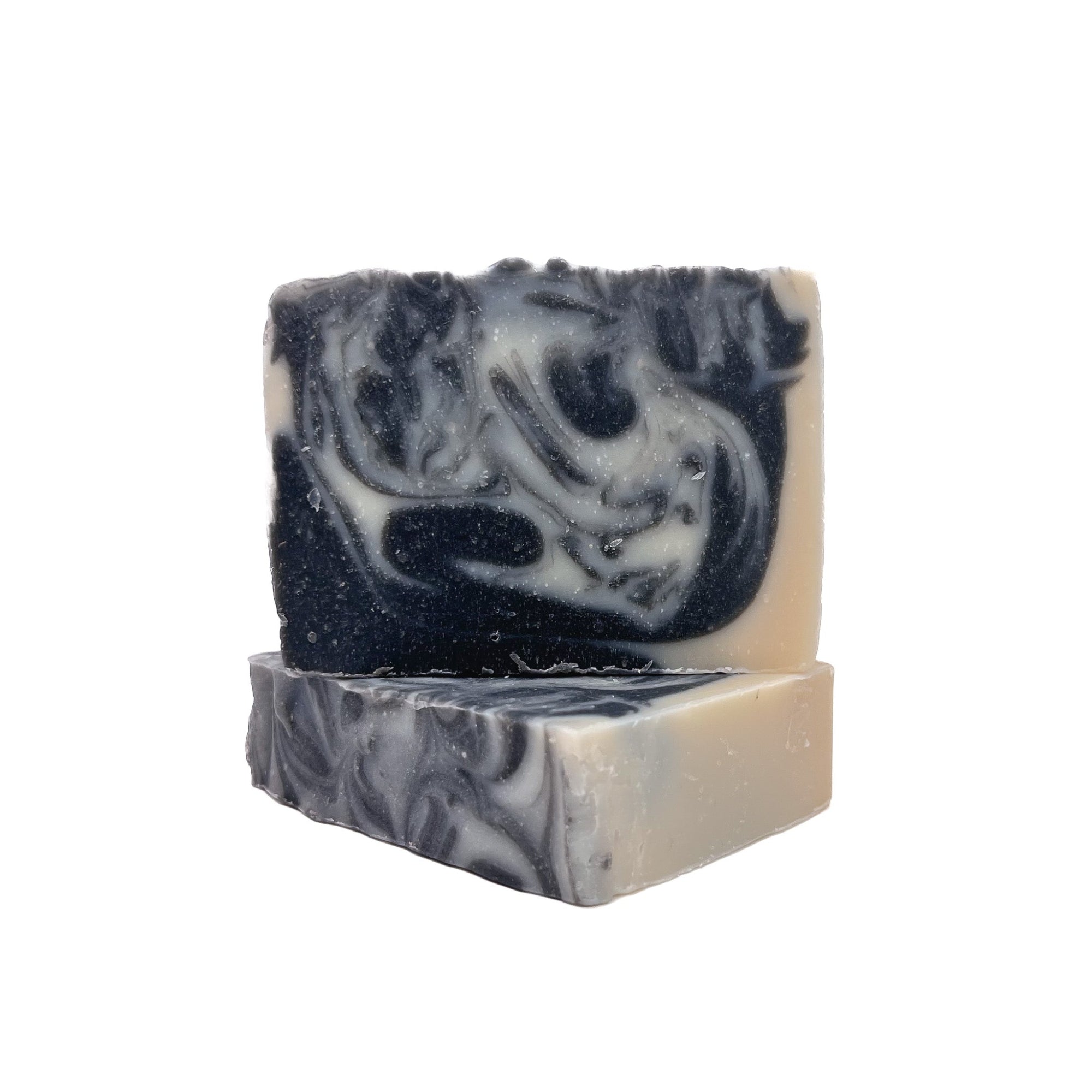 Two bars of Rusted Acre Soap Company's Tuxedo soap. Colored charcoal black and natural white swirled. One lying flat one upright.
