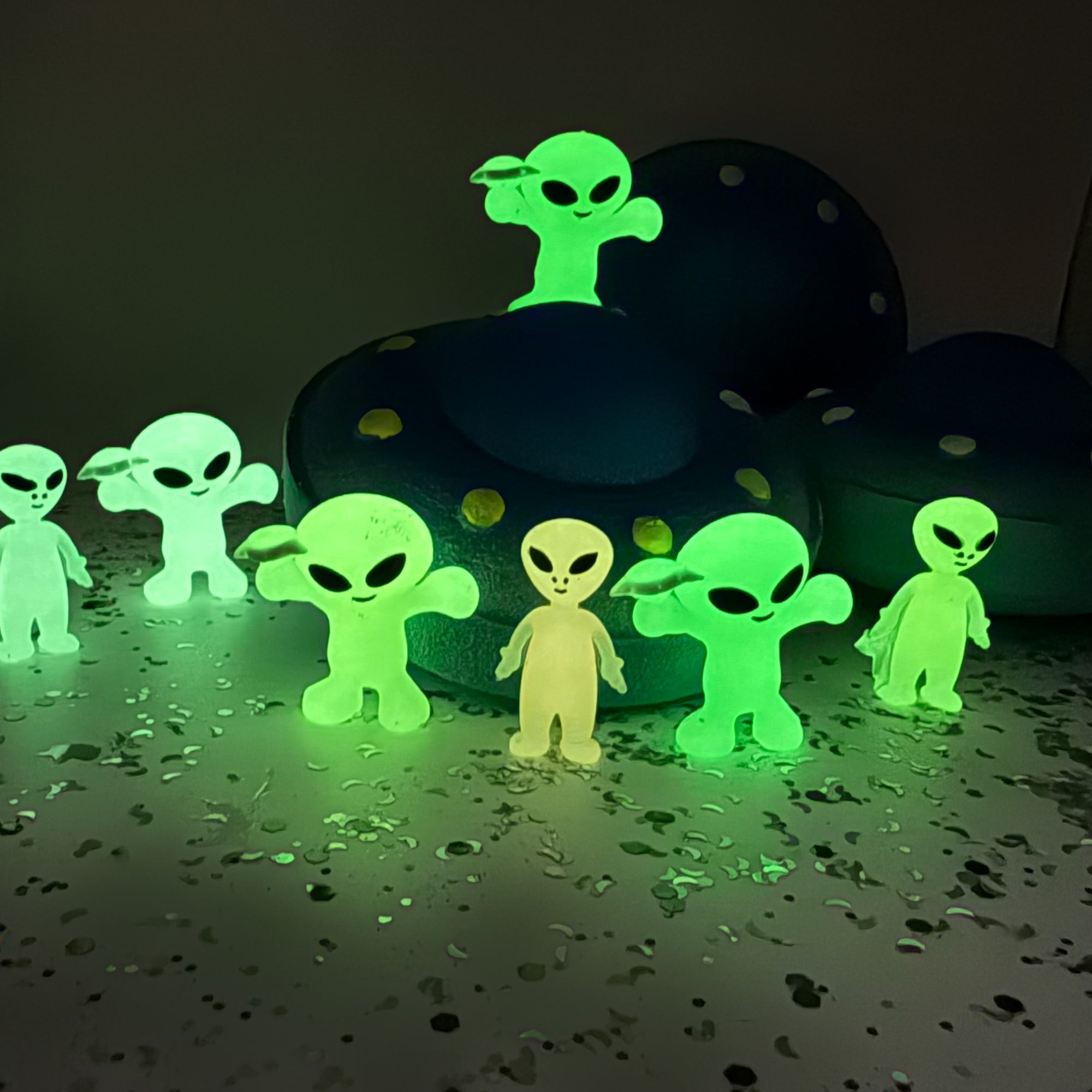 Glowing green alien figures with a UFO bath bomb on a dark surface