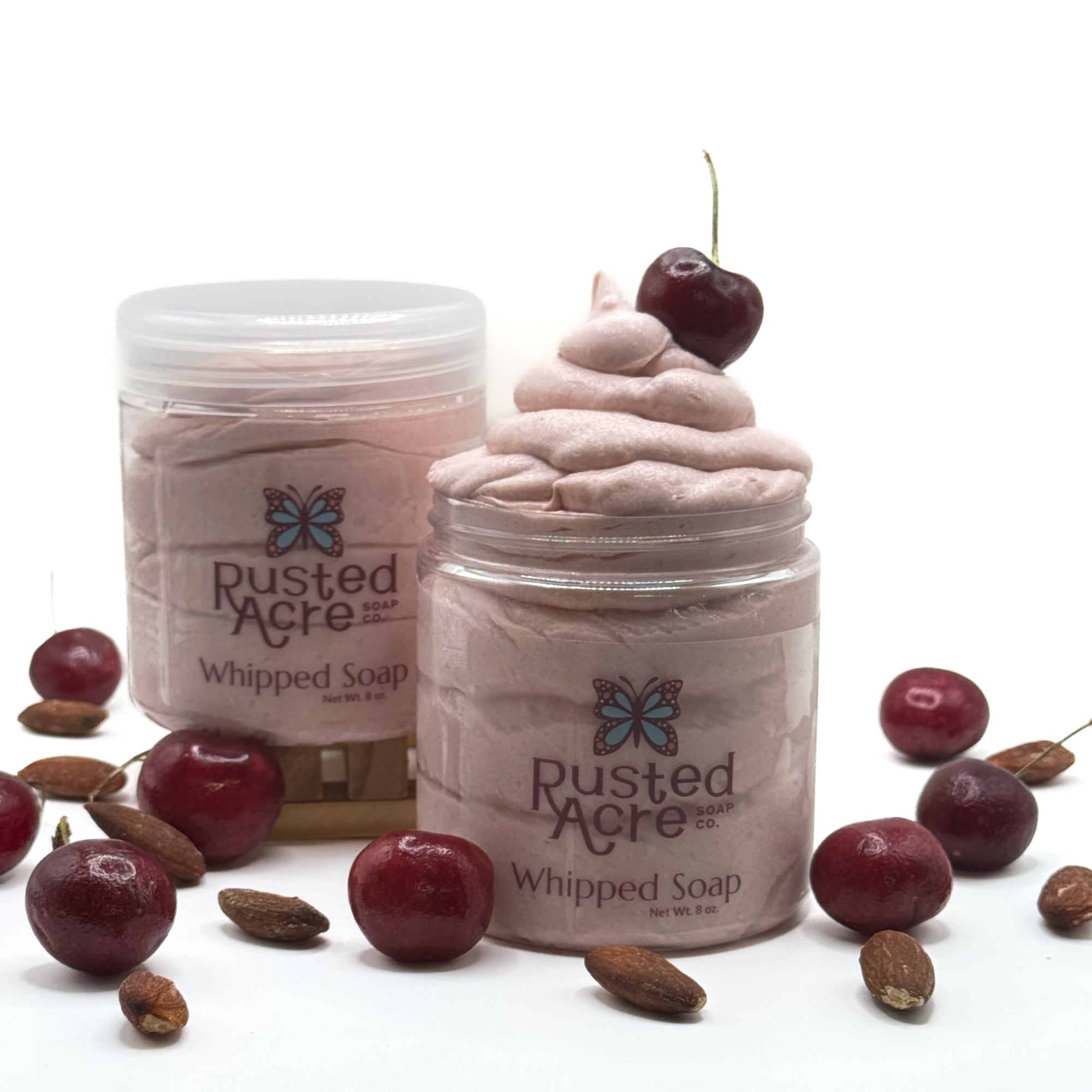 Two jars of Rusted Acre Soap Co's cherry almond whipped soap with cherries and almonds on a white background.