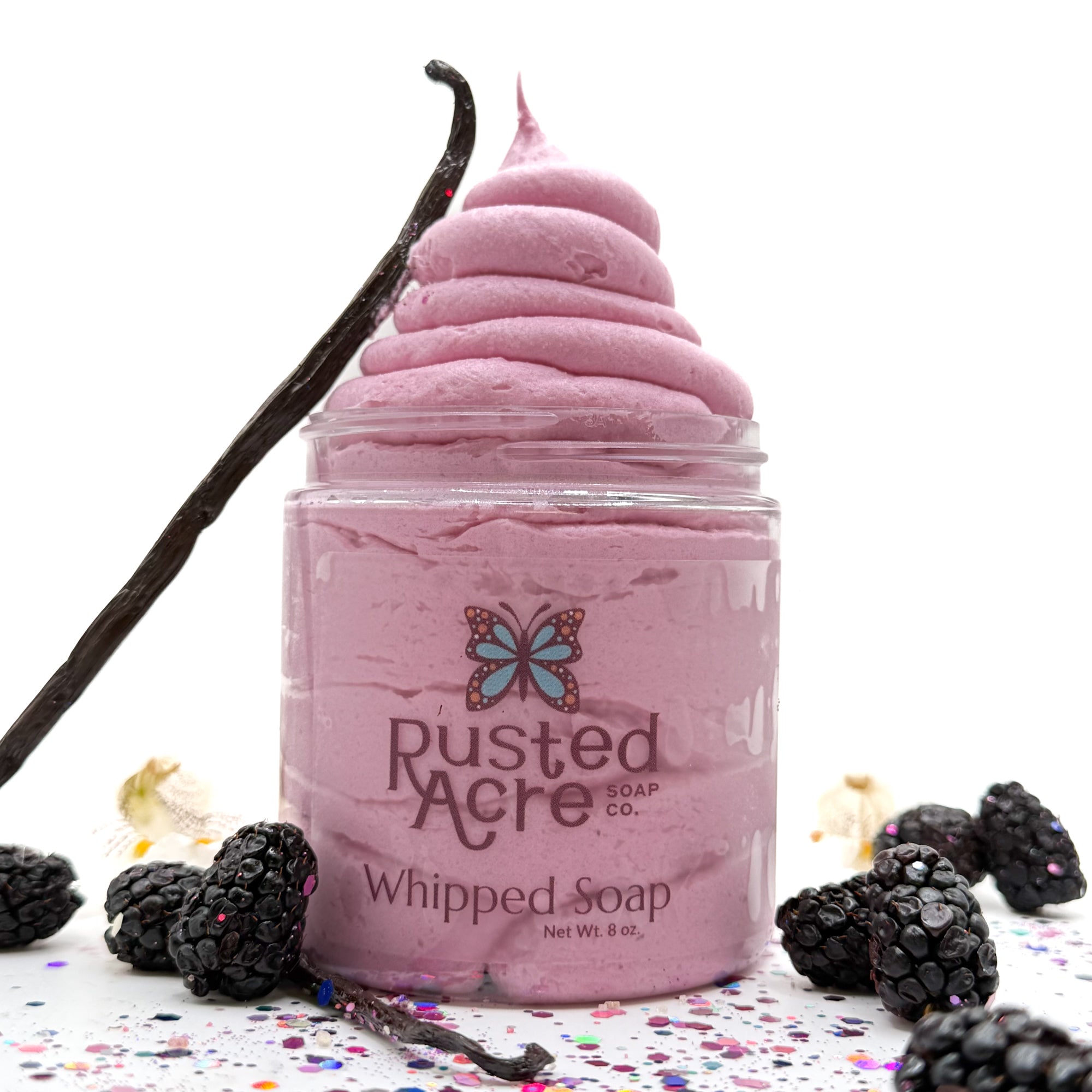 One jar of pink raspberry vanilla whipped soap in a jar with blackberries and a vanilla bean on a light background