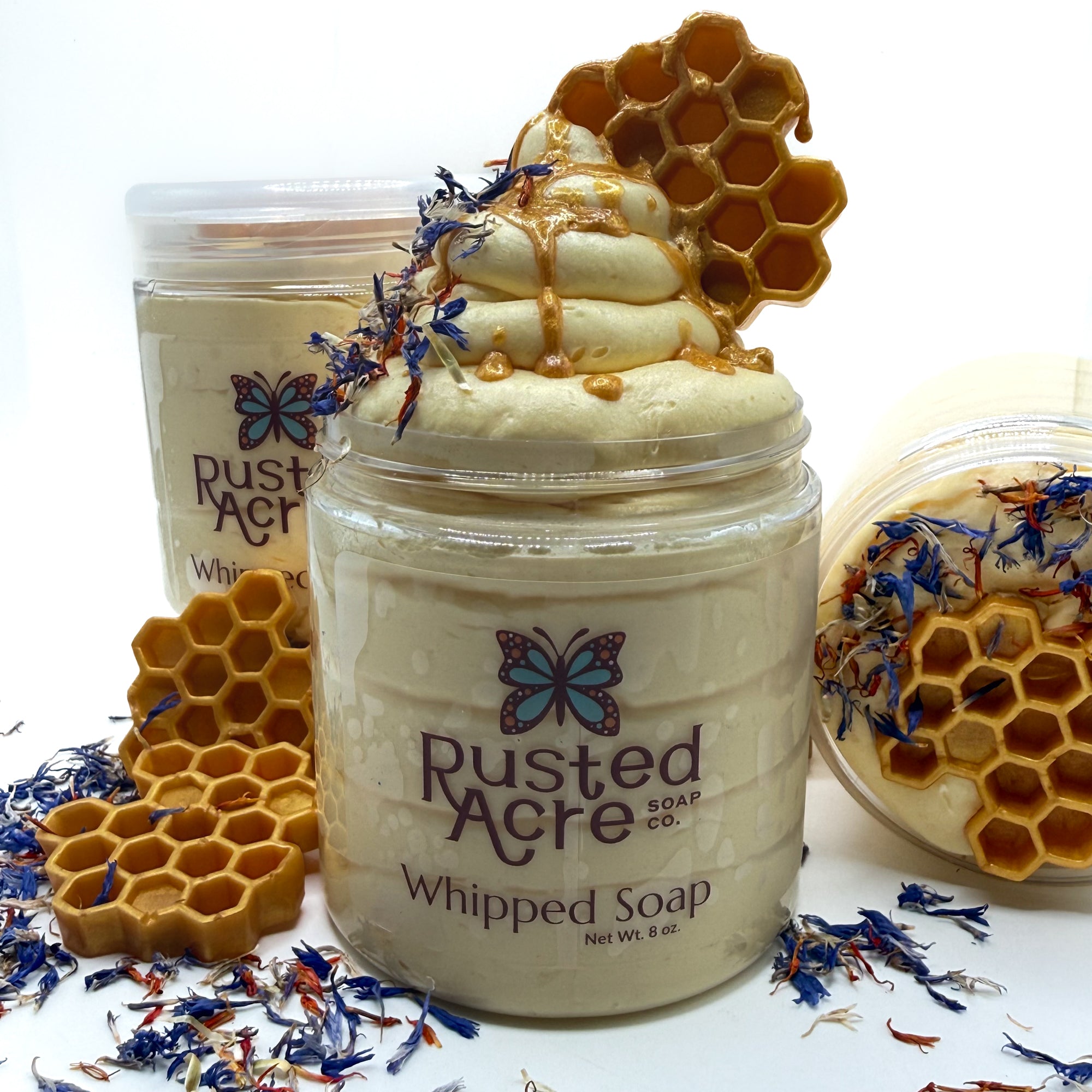 Jar of Rusted Acre wildflower honey whipped soap with honeycomb and floral decorations on a white background