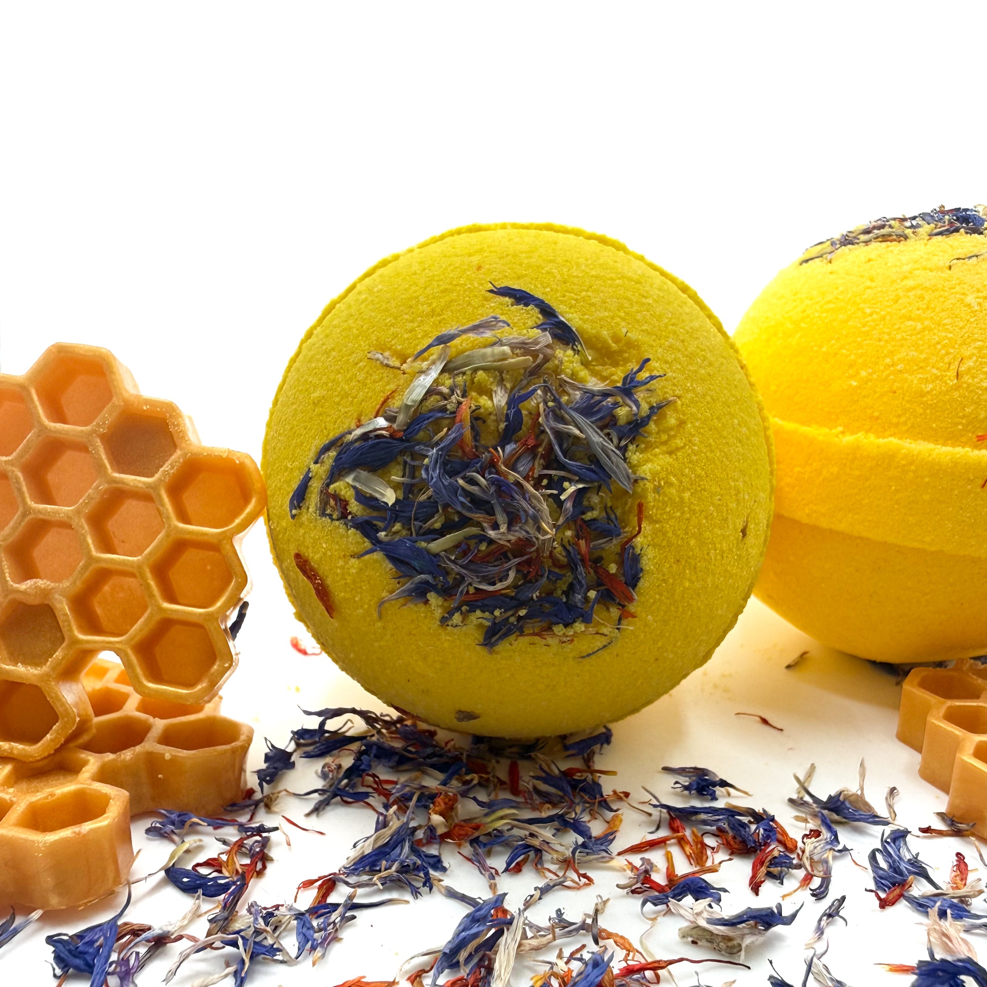A round yellow bath bomb with red and blue cornflower petals embedded in the top.