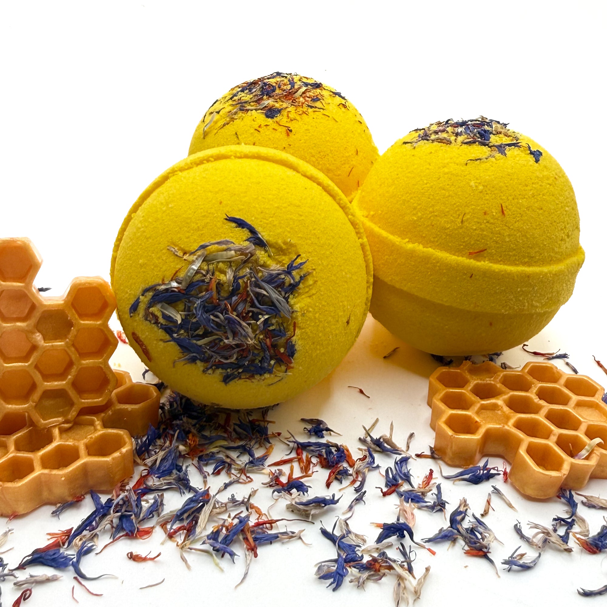 Three yellow wildflower and honey bath bomb with embedded wildflowers showing different view points on a white background with wildflowers.