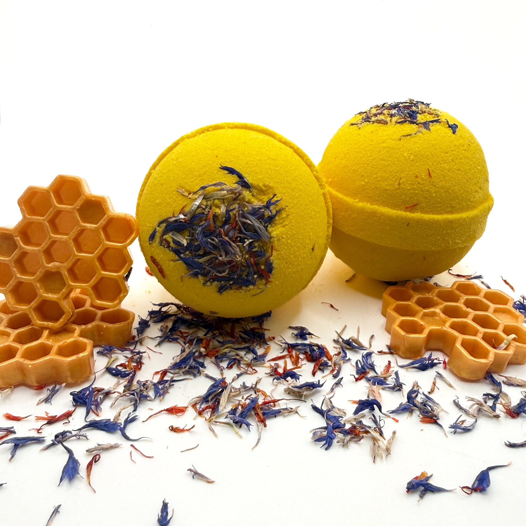 Two yellow wildflower and honey bath bomb with embedded wildflowers showing the front and side on a white background with wildflowers.