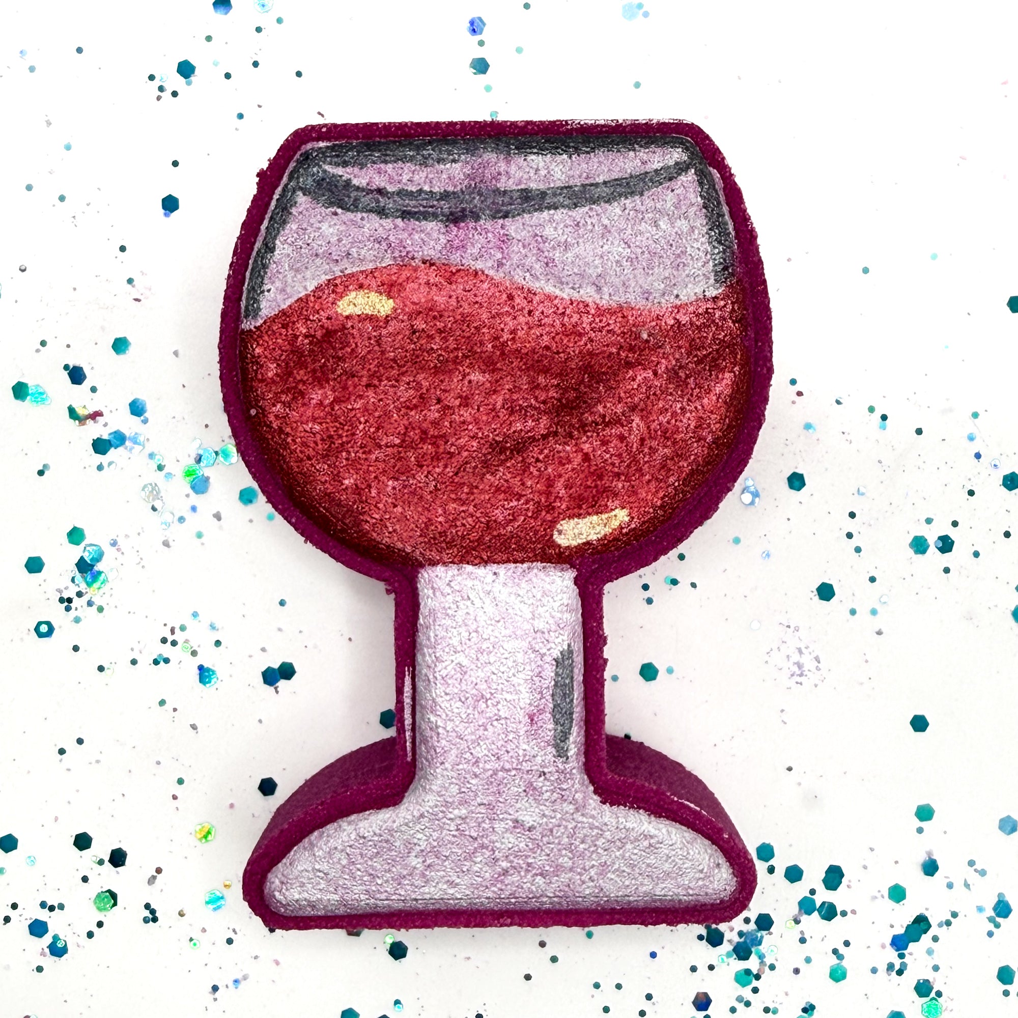 Burgundy colored wine glass shaped bath bomb with hand painted silver stem and gray accent. The wine is hand painted deep burgundy with illusion of swirling in the glass. Displayed on a rustic wooden background.