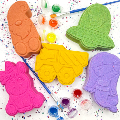 5 handmade bath bombs, a orange gnome, a green spaceship, a yellow dump truck, a pink unicorn, and a purple mermaid.