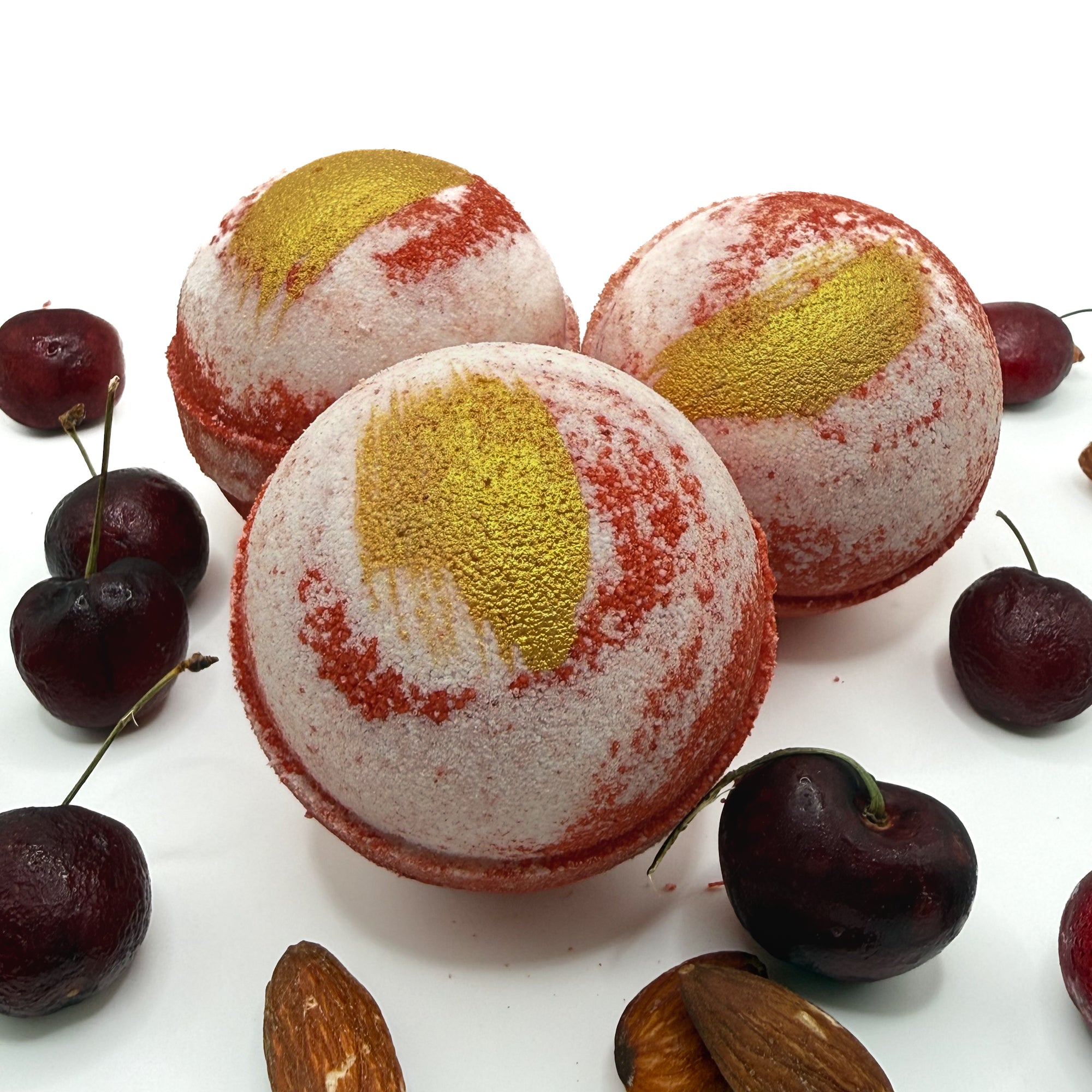 3 handmade cherry almond bath bombs by Rusted Acre Soap Co with cherry and almond decorations on a white background.