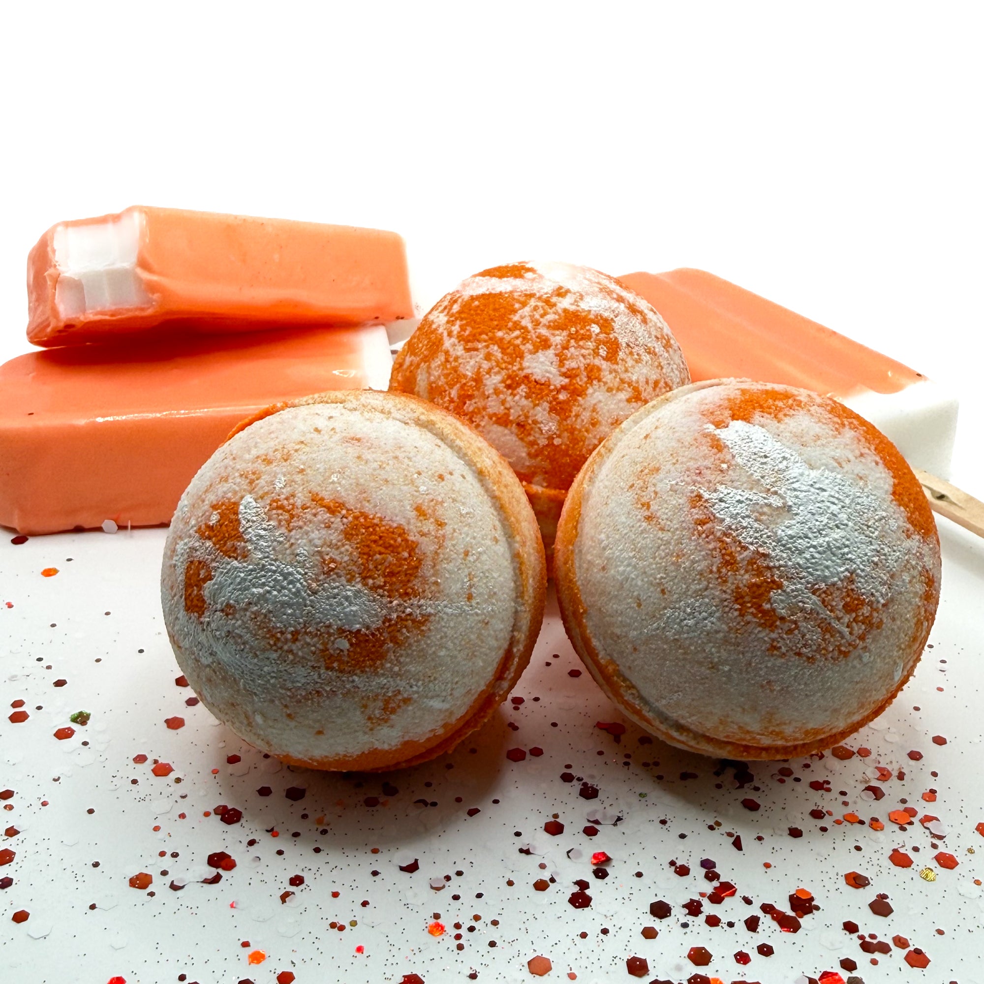3 orange and white bath bombs handmade by Rusted Acre Soap Co with orange ice cream soap bars on a white background.