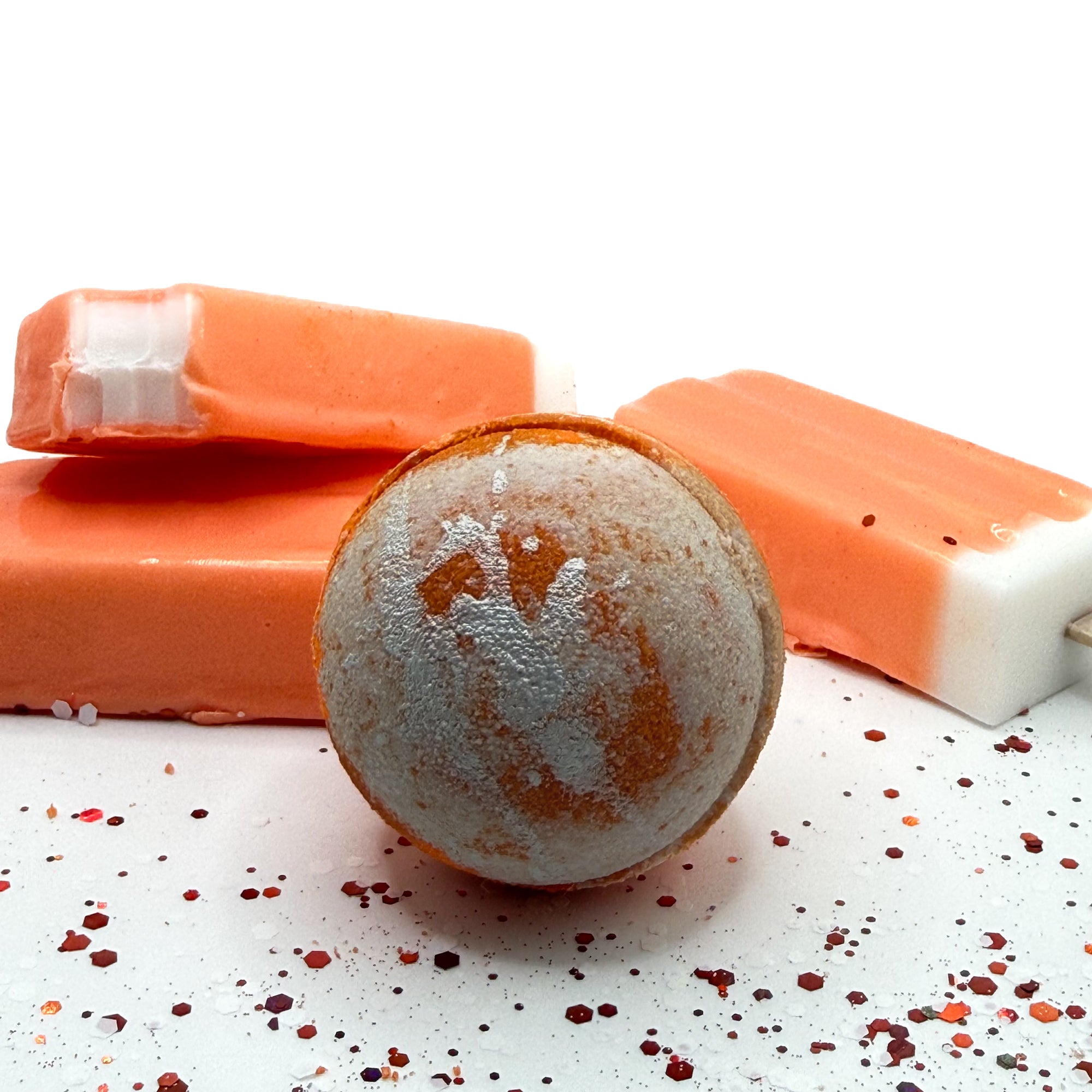 A handmade orange and white swirled bath bomb with orange and white ice cream soap bars, by Rusted Acre Soap Co.