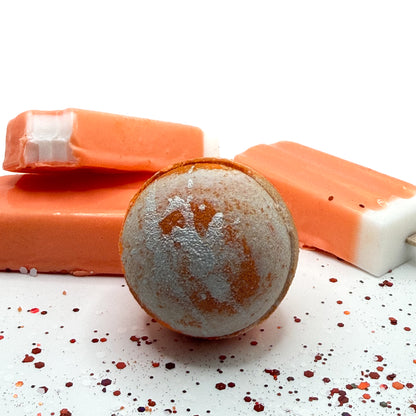 A handmade orange and white swirled bath bomb with orange and white ice cream soap bars, by Rusted Acre Soap Co.