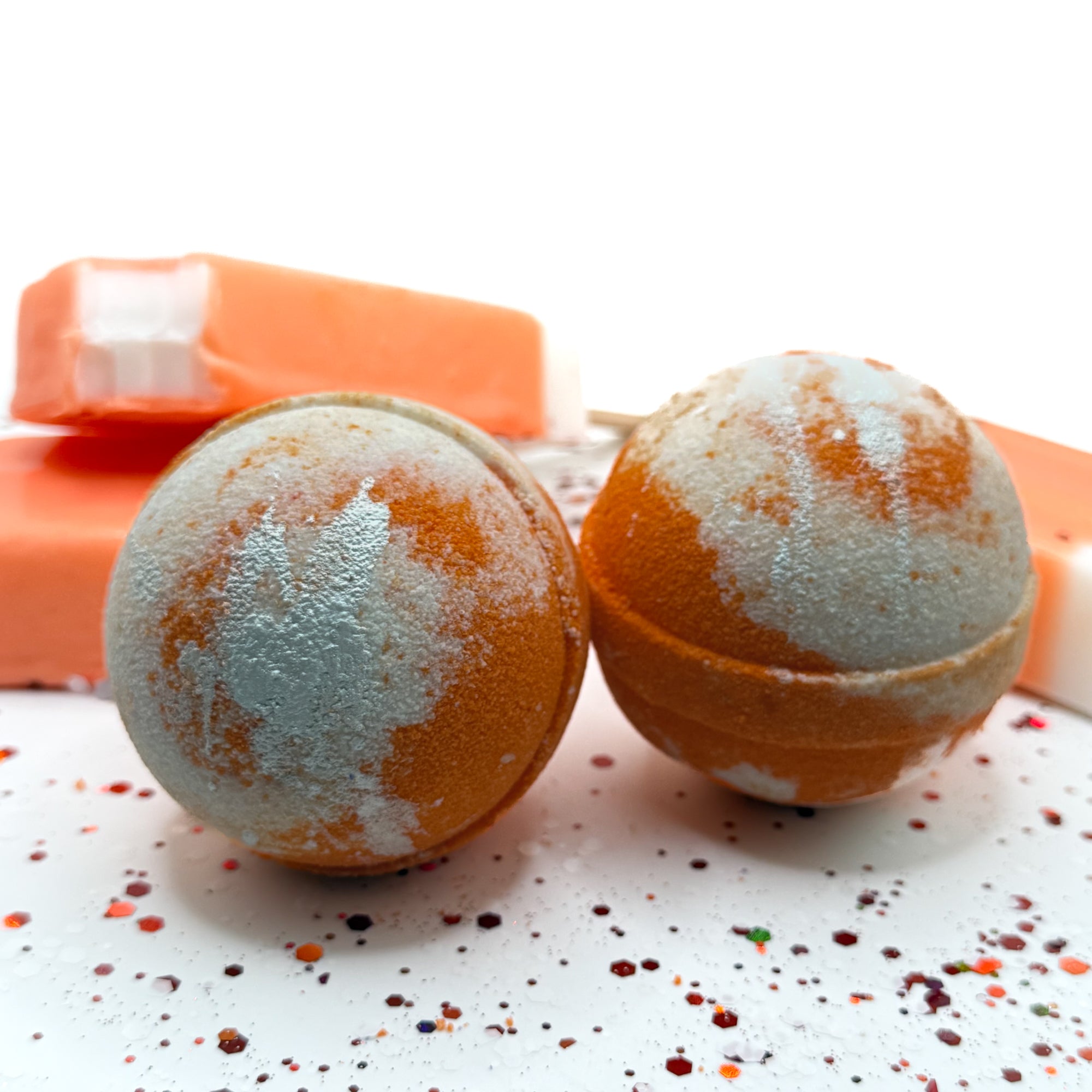 2 handmade orange bath bombs with white swirls and orange ice cream bars in the background.