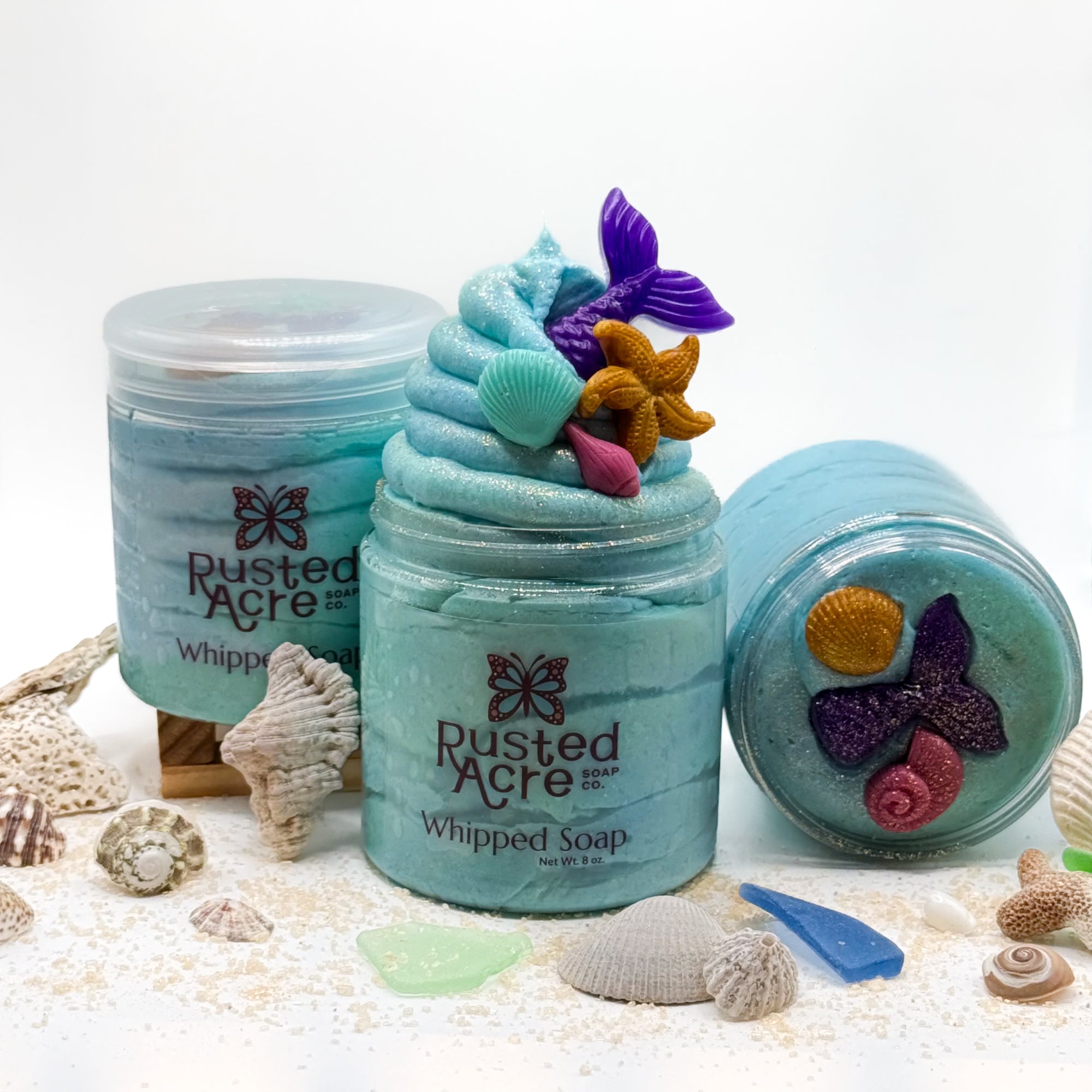Three jars of Rusted Acre mermaid kiss whipped soap surrounded with seashells.