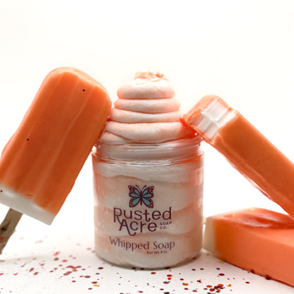 Jar of Rusted Acre orange dream whipped soap and 3 orange ice cream bars. One is bitten.