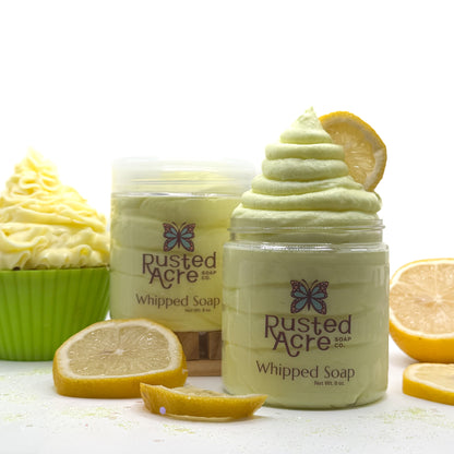 Two jars of Rusted Acre lemon cupcake whipped soap with lemon slices and a cupcake on a white background.