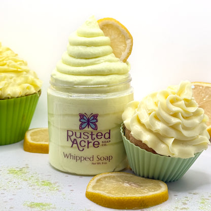 Jar of Rusted Acre lemon cupcake whipped soap with lemon slices and cupcakes on a white background.
