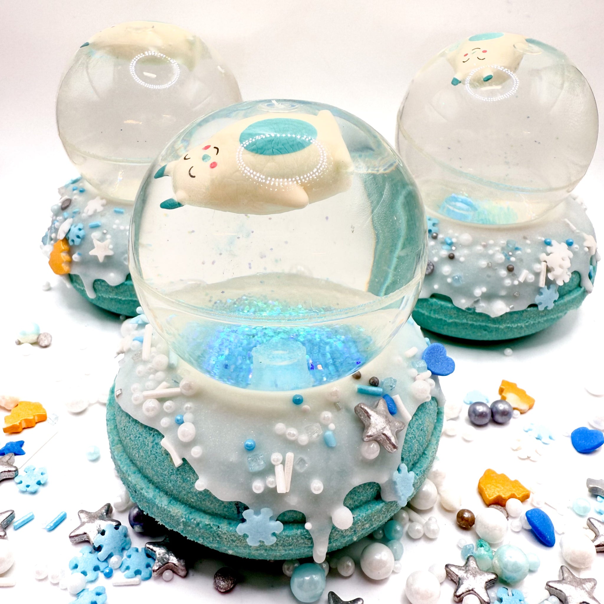 Three abominable snowman snow globe bath bombs on a white background with blue, silver, and gold sprinkles.