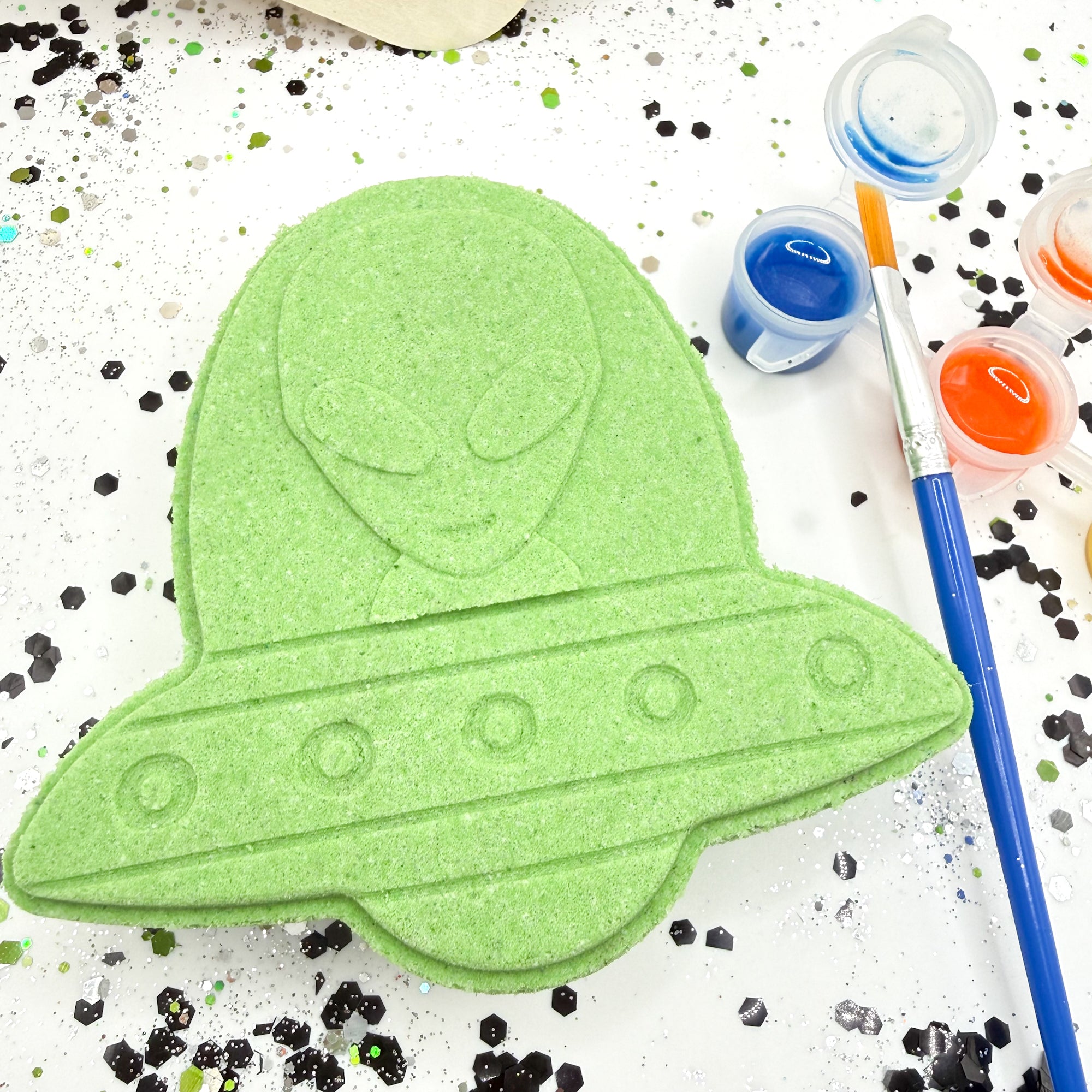 Green alien UFO paint your own bath bomb with paint containers and brushes on a white background