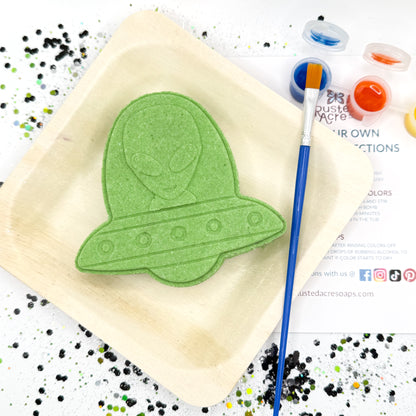 Green paint your own alien bath bomb kit on a wood plate with paint supplies.