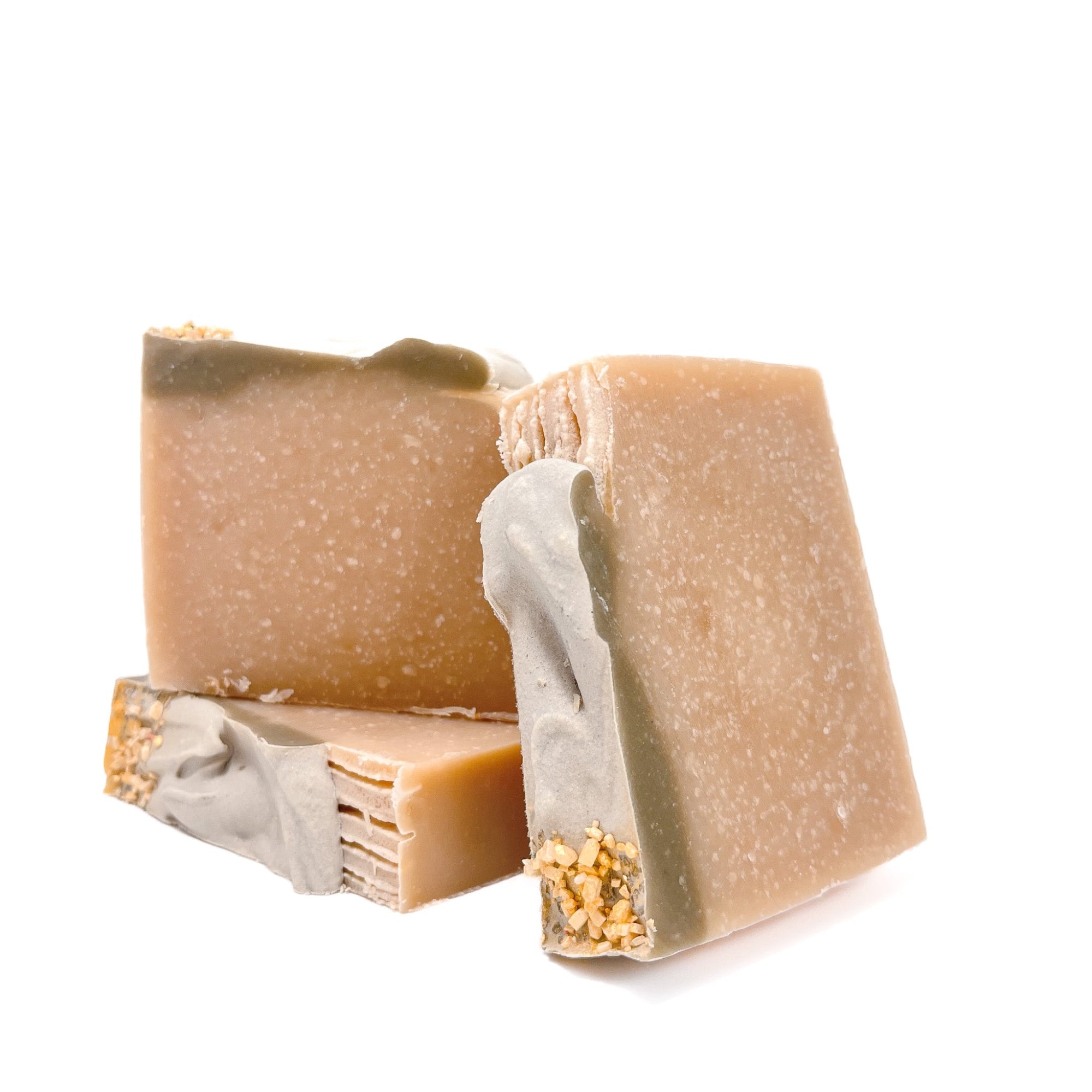 Three bars of natural-colored handmade soap, topped with a bit of green soap, and gold epsom salt dusted with gold mica.